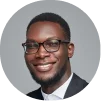 Smiling man wearing glasses and a suit jacket against a gray background.