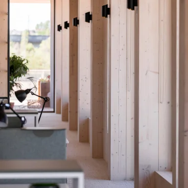 Modern office corridor with wooden walls, black wall lights, and a desk lamp by a plant.