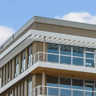 Top corner of a modern building with large glass windows and white balcony railings under blue sky.