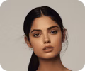 Portrait of a young woman with long black hair and natural makeup against a plain background.