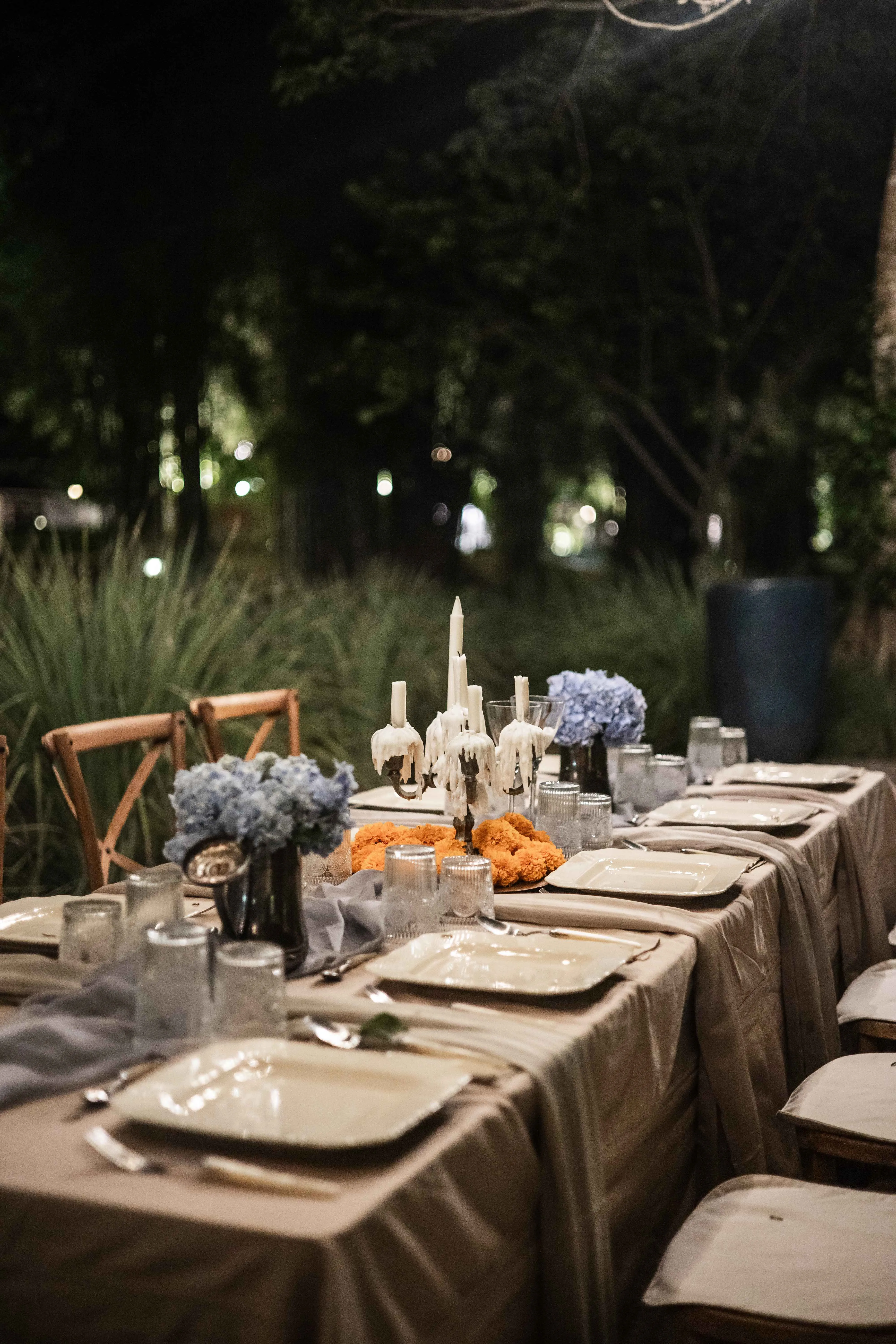 A candlelit outdoor dining table setup with blue hydrangeas and marigolds for the evening cacao ceremony and shared dinner at Campuhan retreat.