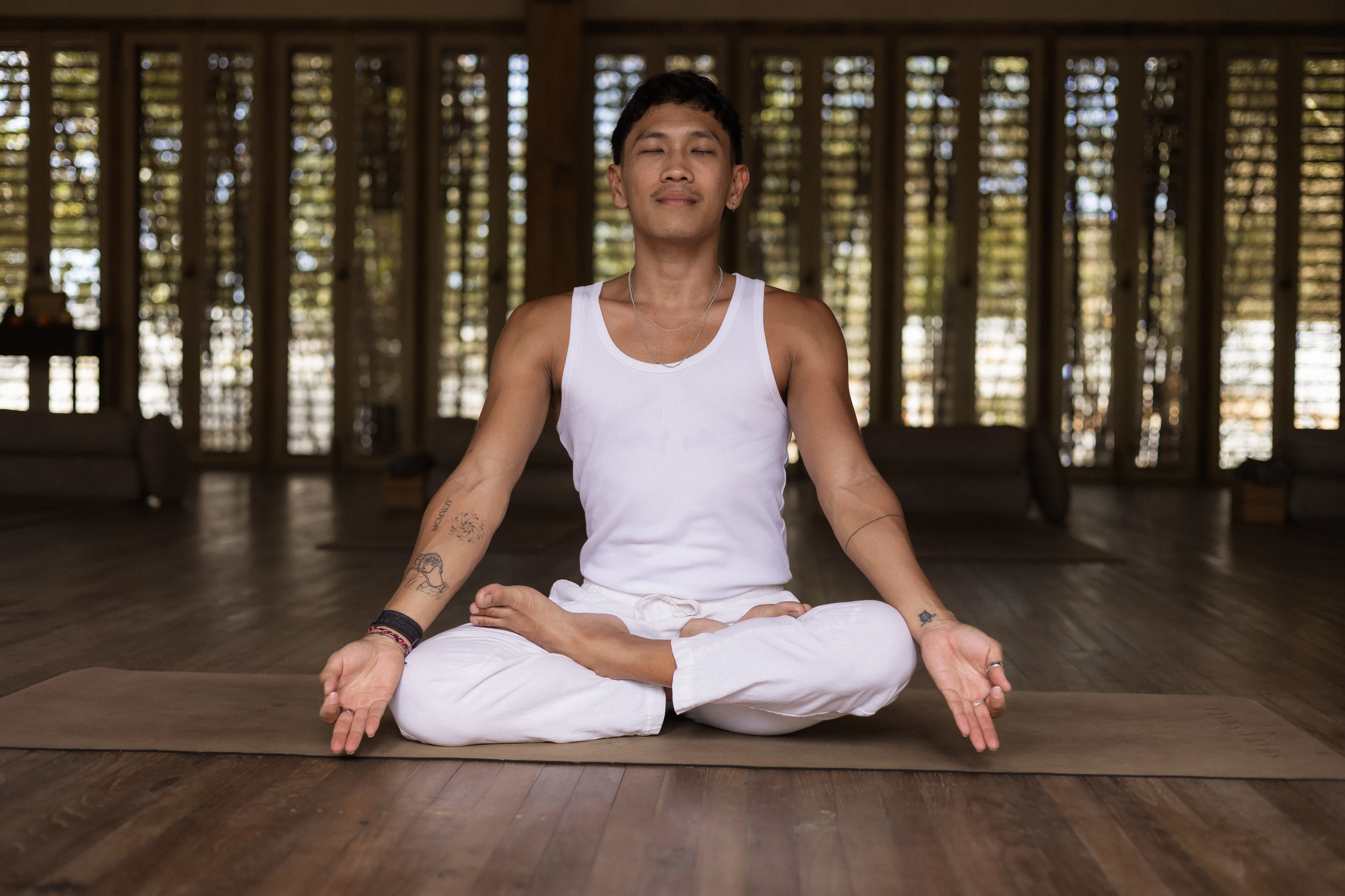 A male practitioner sitting in a crossed-leg Lotus meditation pose on a mat inside the wooden shala at The Shaba Shala.