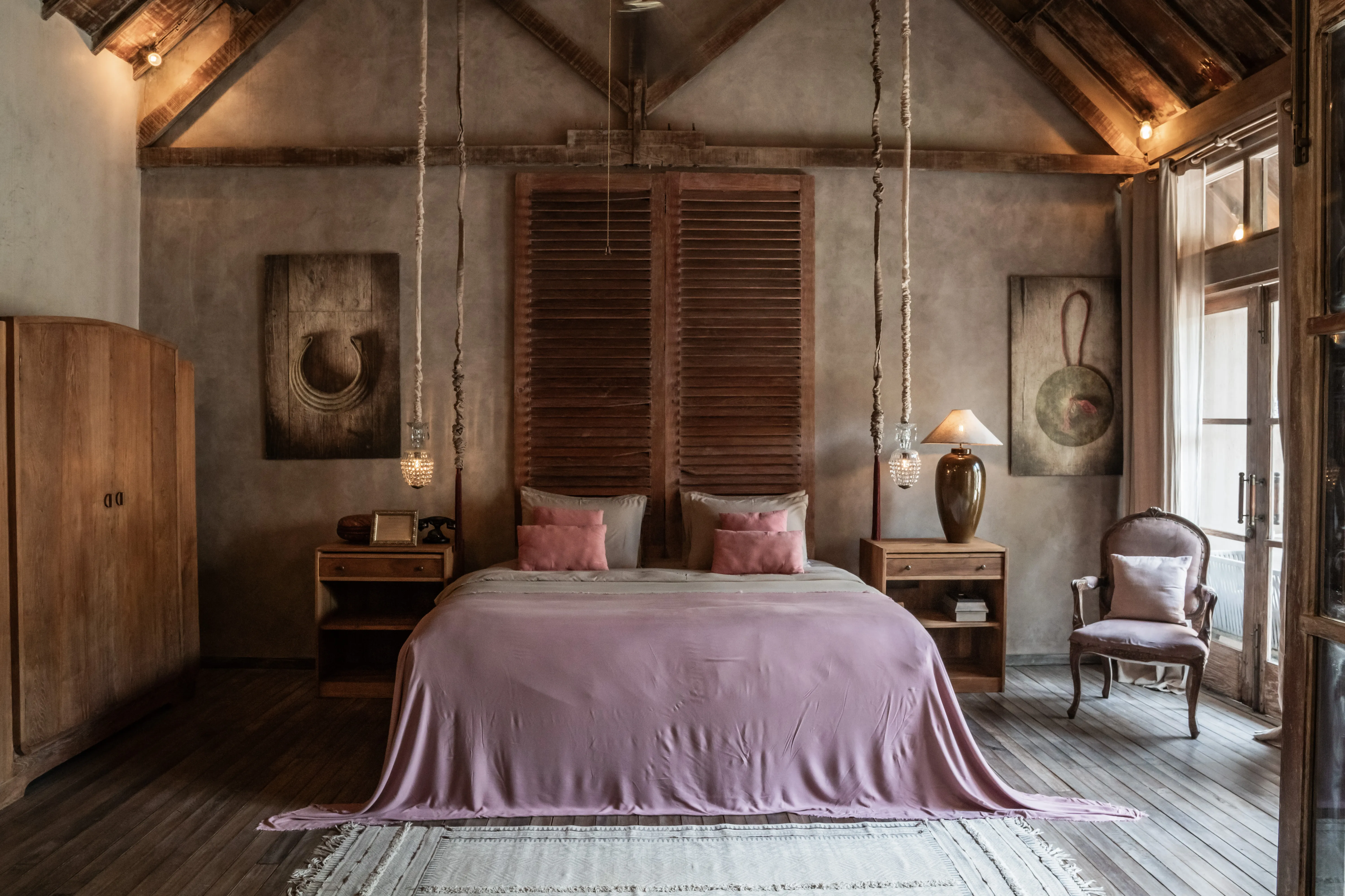 Rustic luxury bedroom at The Shaba Shala with vaulted wooden ceilings, pink linen bedding, and hanging pendant lights.