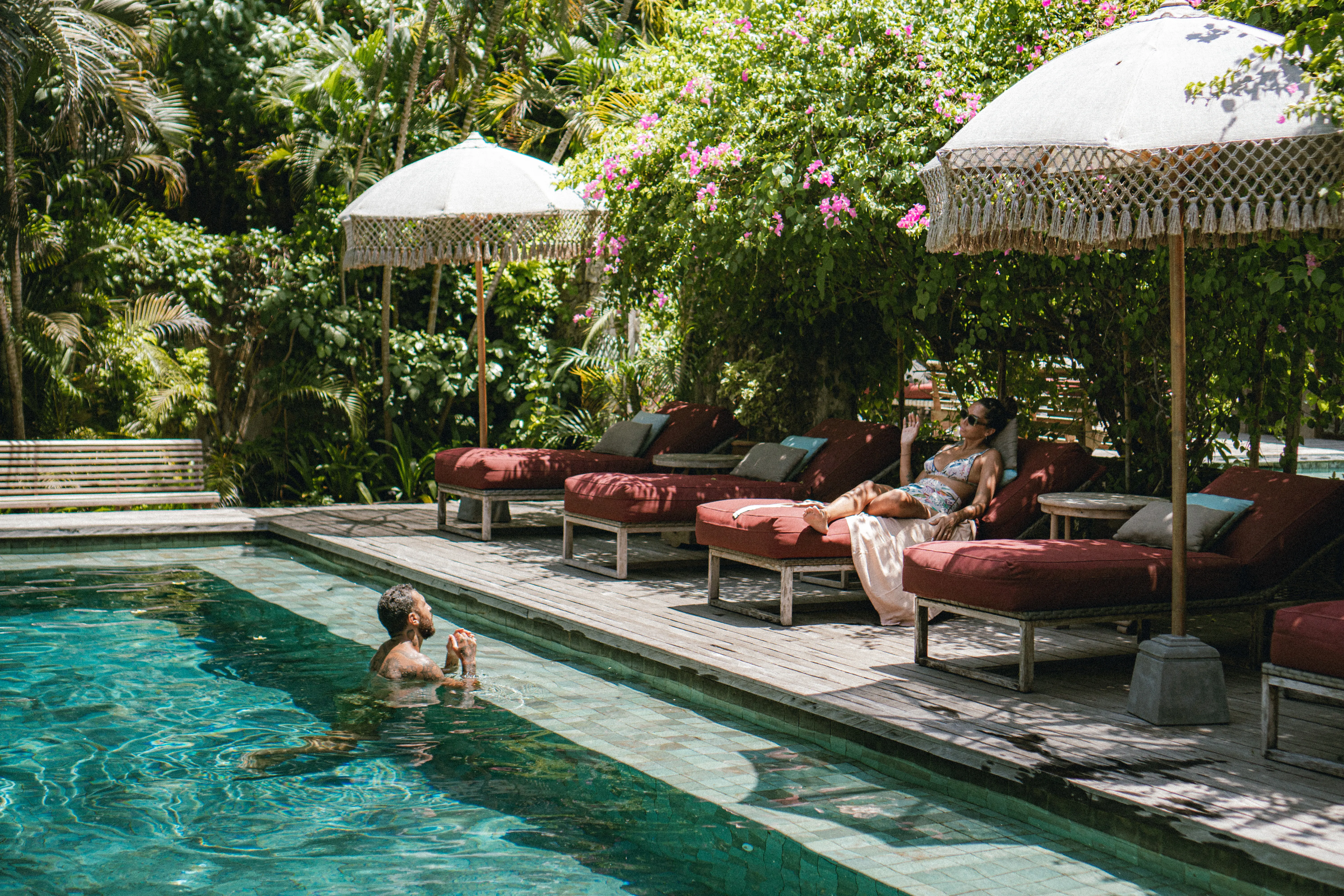 Guests relaxing by a turquoise swimming pool on red cushioned sun loungers with fringe umbrellas at The Shaba Shala.