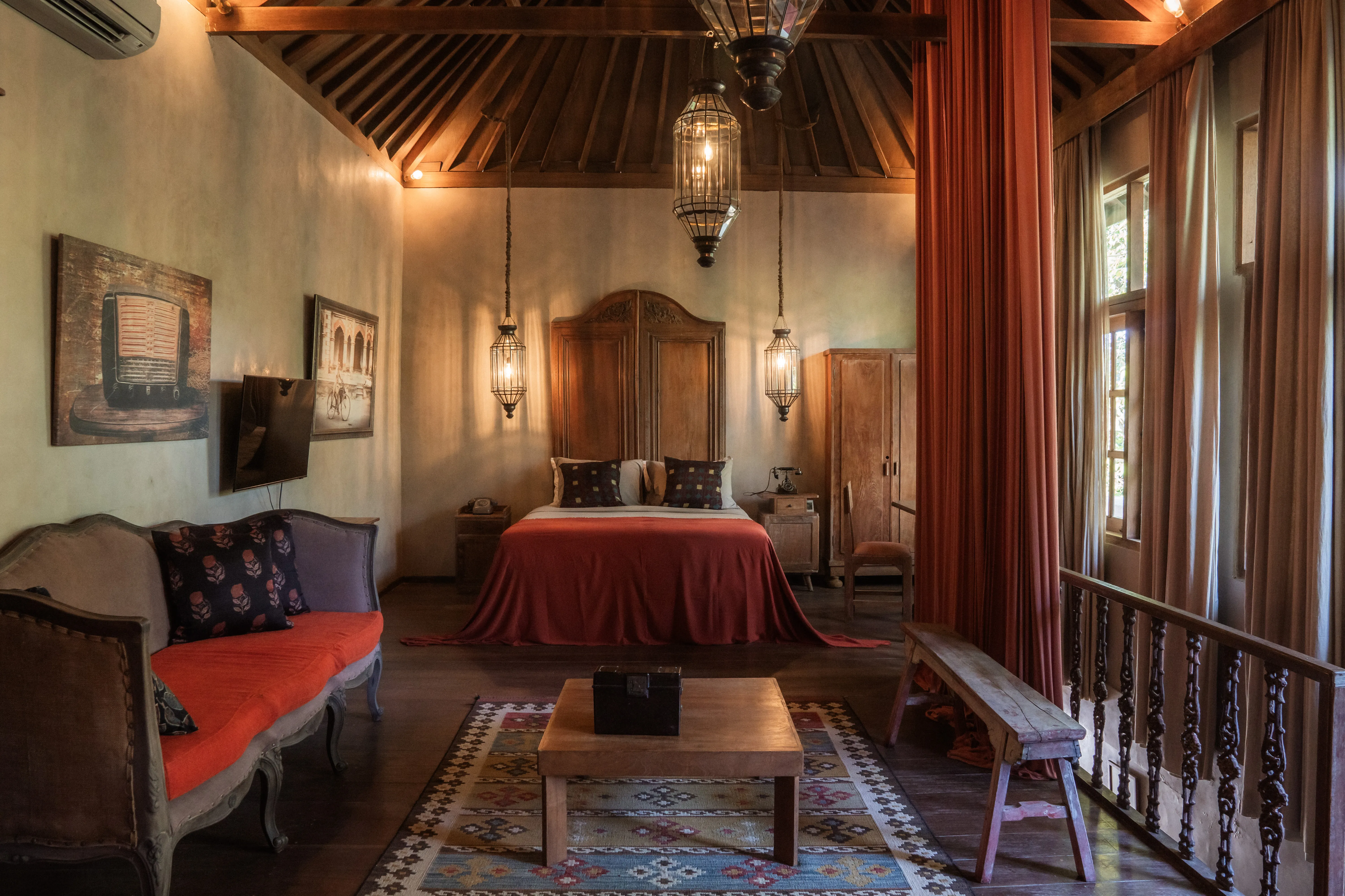 Spacious heritage suite with wooden high-vaulted ceiling, terracotta accent tones, plush seating area, and lantern lights at The Shaba Shala.