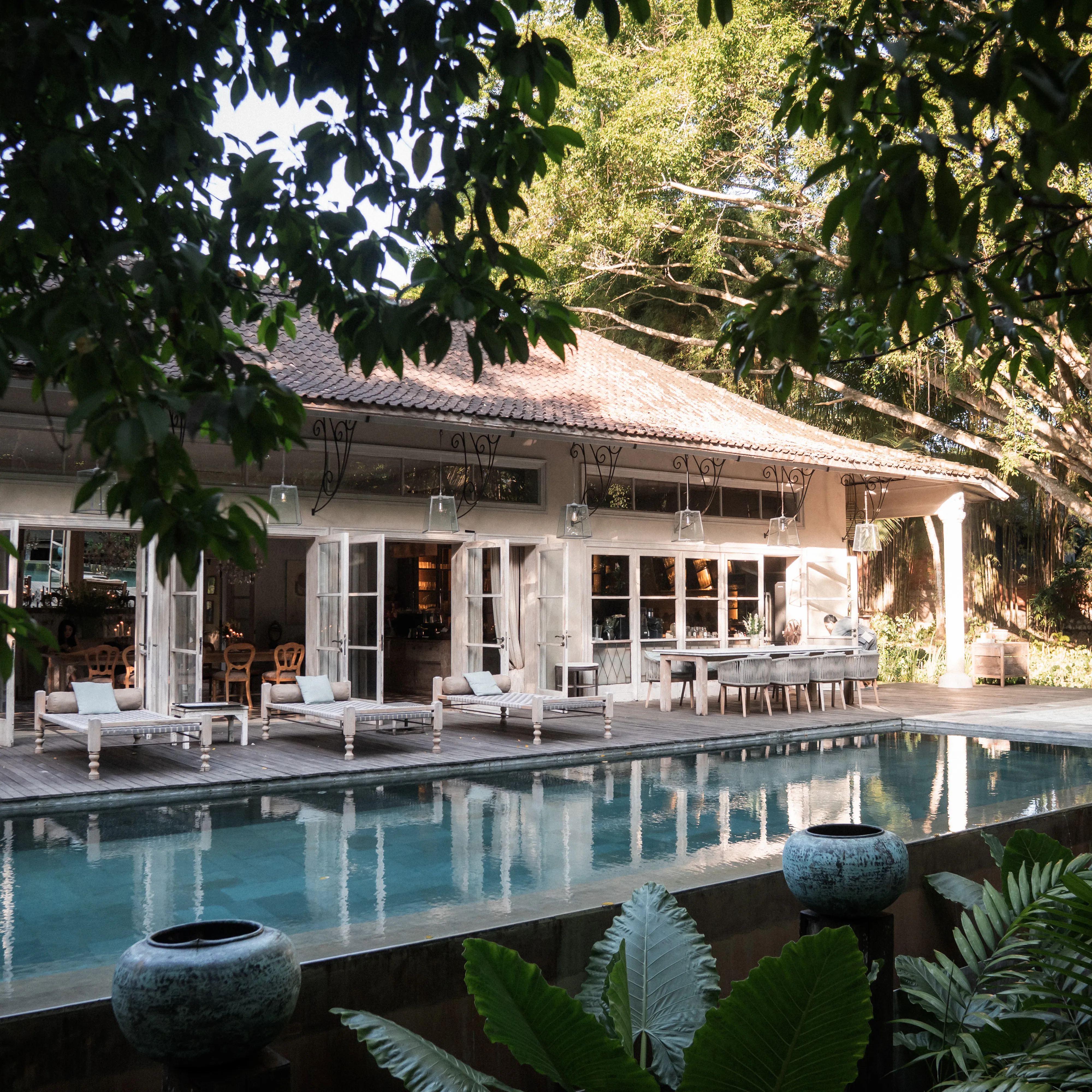 Outdoor swimming pool deck lined with wooden lounge daybeds and an open-air pavilion surrounded by trees at The Shaba Shala.