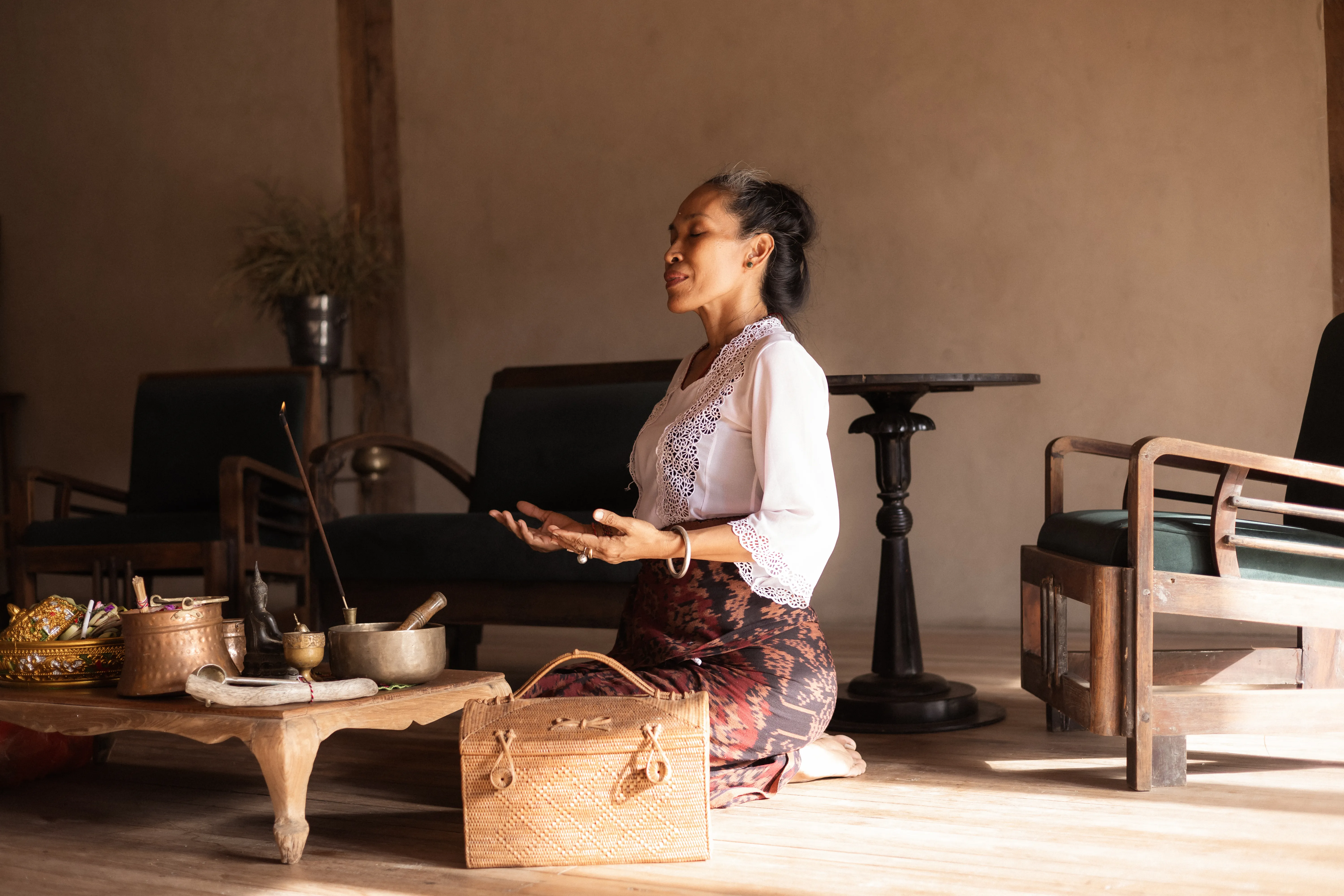 A Balinese healer wearing traditional attire kneeling in meditation next to offerings and a singing bowl at The Shaba Shala.