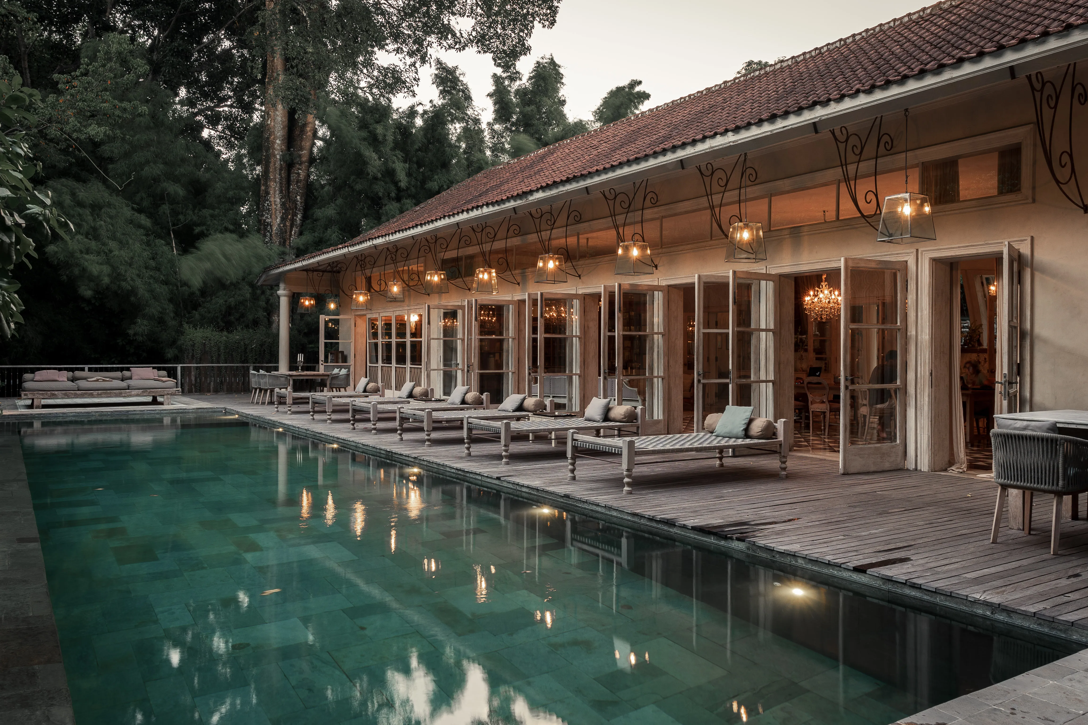 Outdoor swimming pool lined with wooden sunbeds under warm hanging lanterns outside the main building at The Shaba Shala.