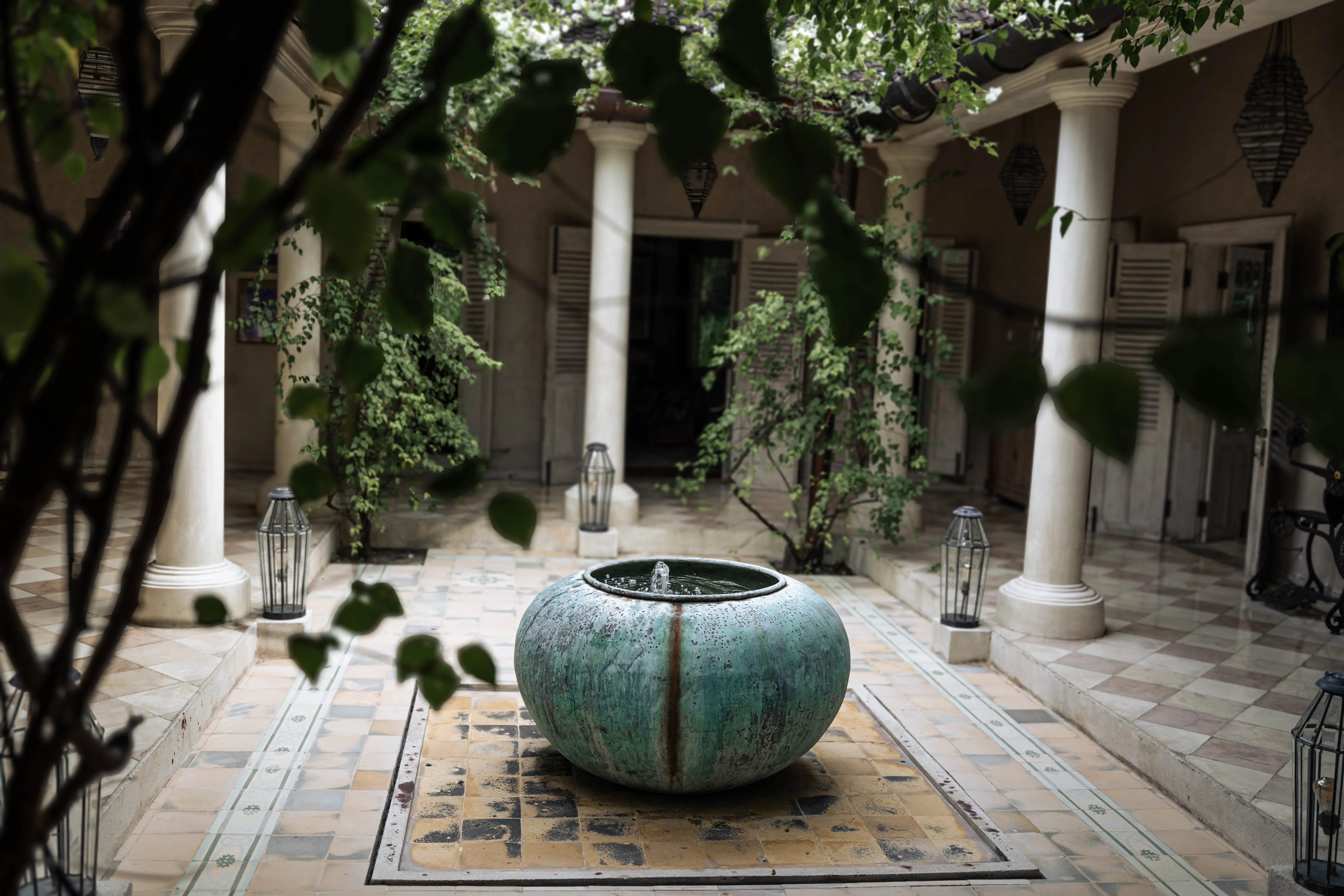 Turquoise pottery water fountain set in a tiled courtyard surrounded by white pillars at The Shaba Shala.