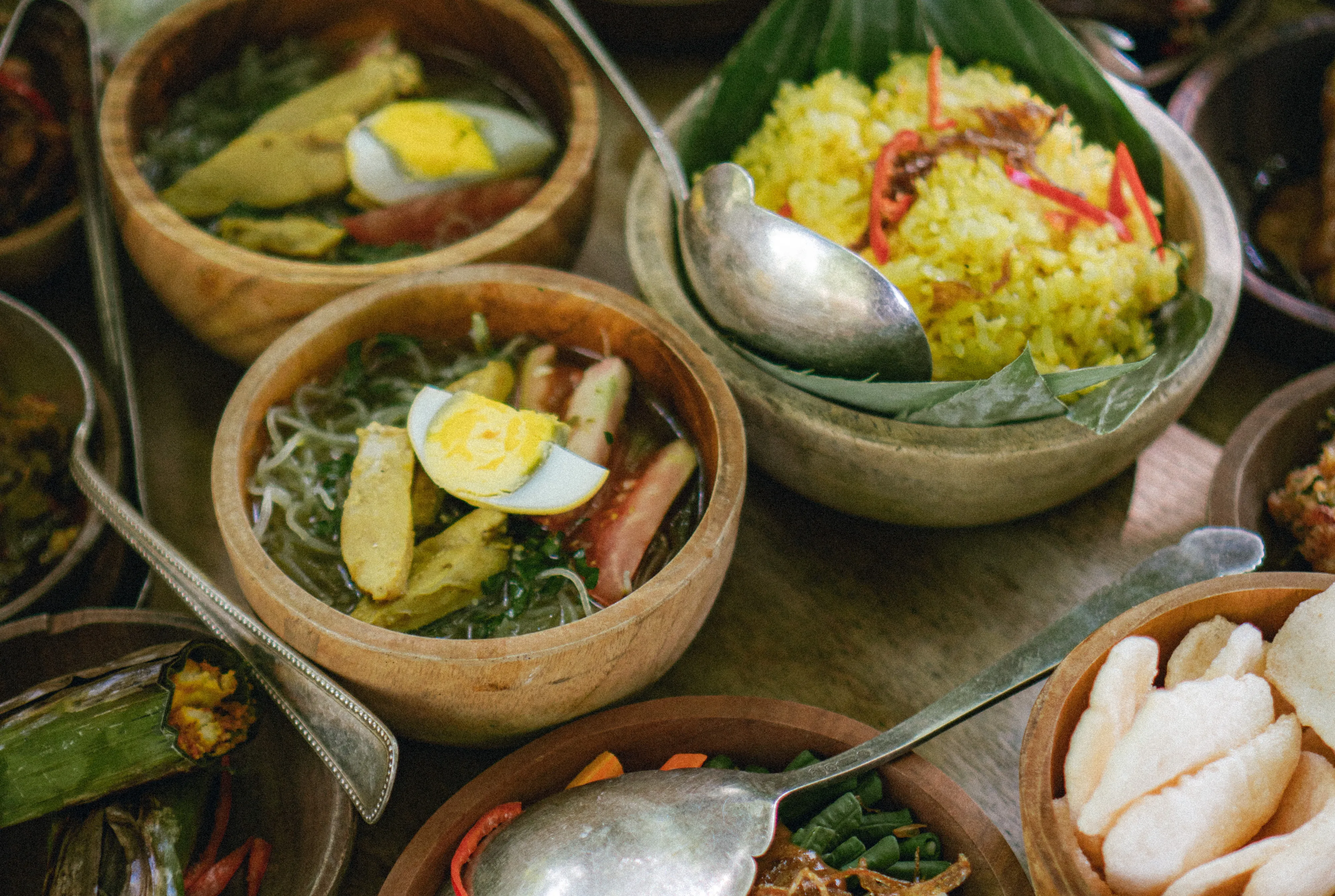 Wooden bowls of yellow rice, Indonesian soto soup, and traditional side dishes served at The Shaba Shala.