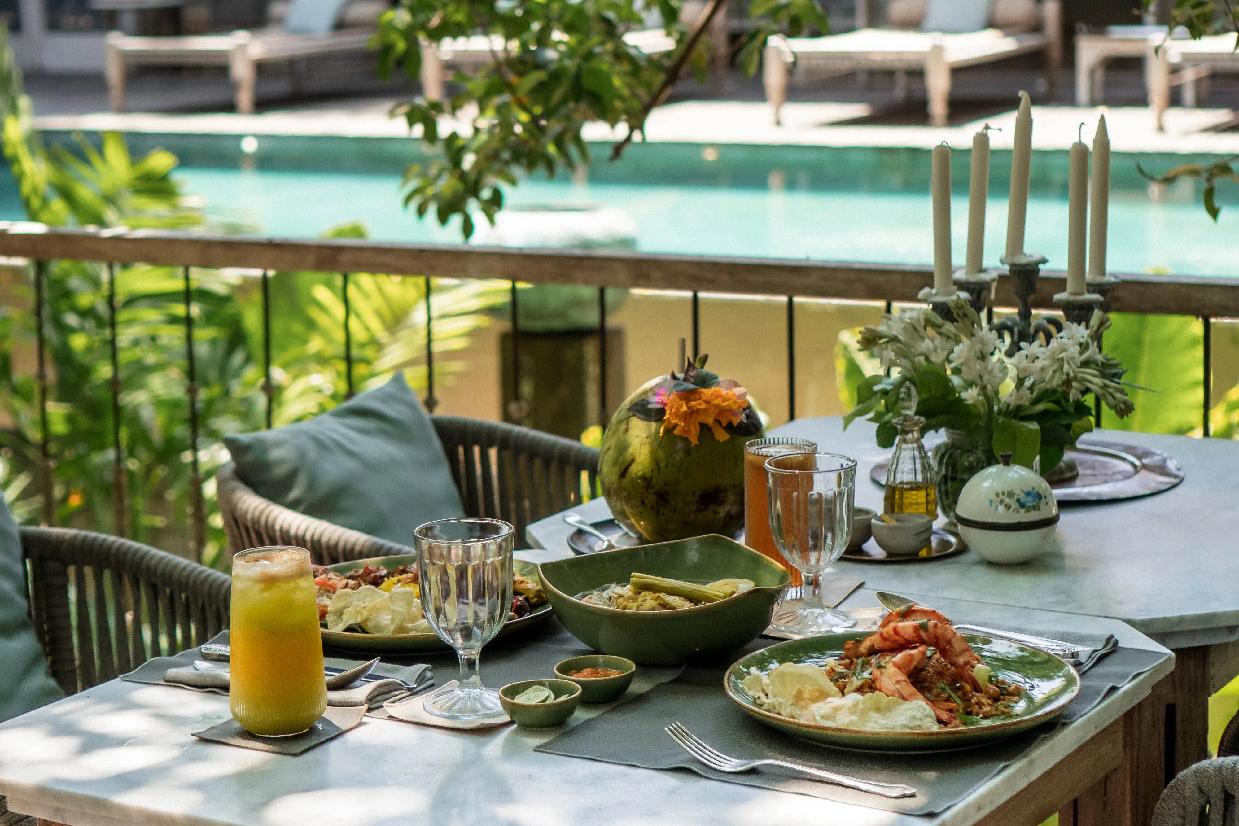Outdoor dining table at The Shaba Shala set with fresh juice, grilled prawns, traditional dishes, and fresh coconut overlooking a swimming pool.