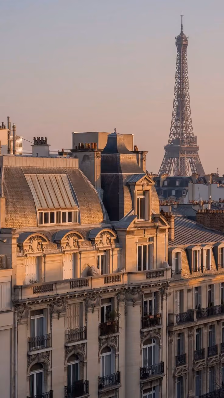 Toits et façades de bâtiments haussmanniens avec la Tour Eiffel en arrière-plan au coucher du soleil.
