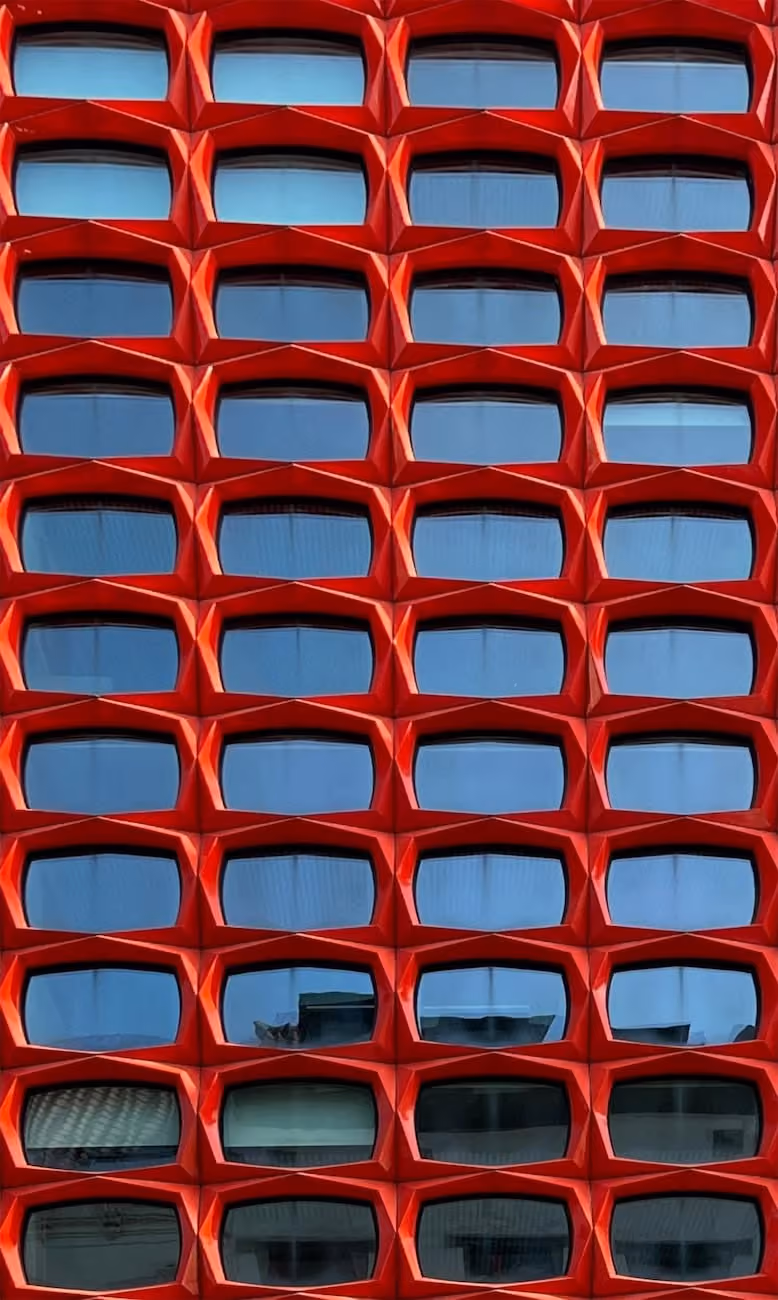Façade d’un bâtiment avec des fenêtres encadrées de formes géométriques rouges répétées.