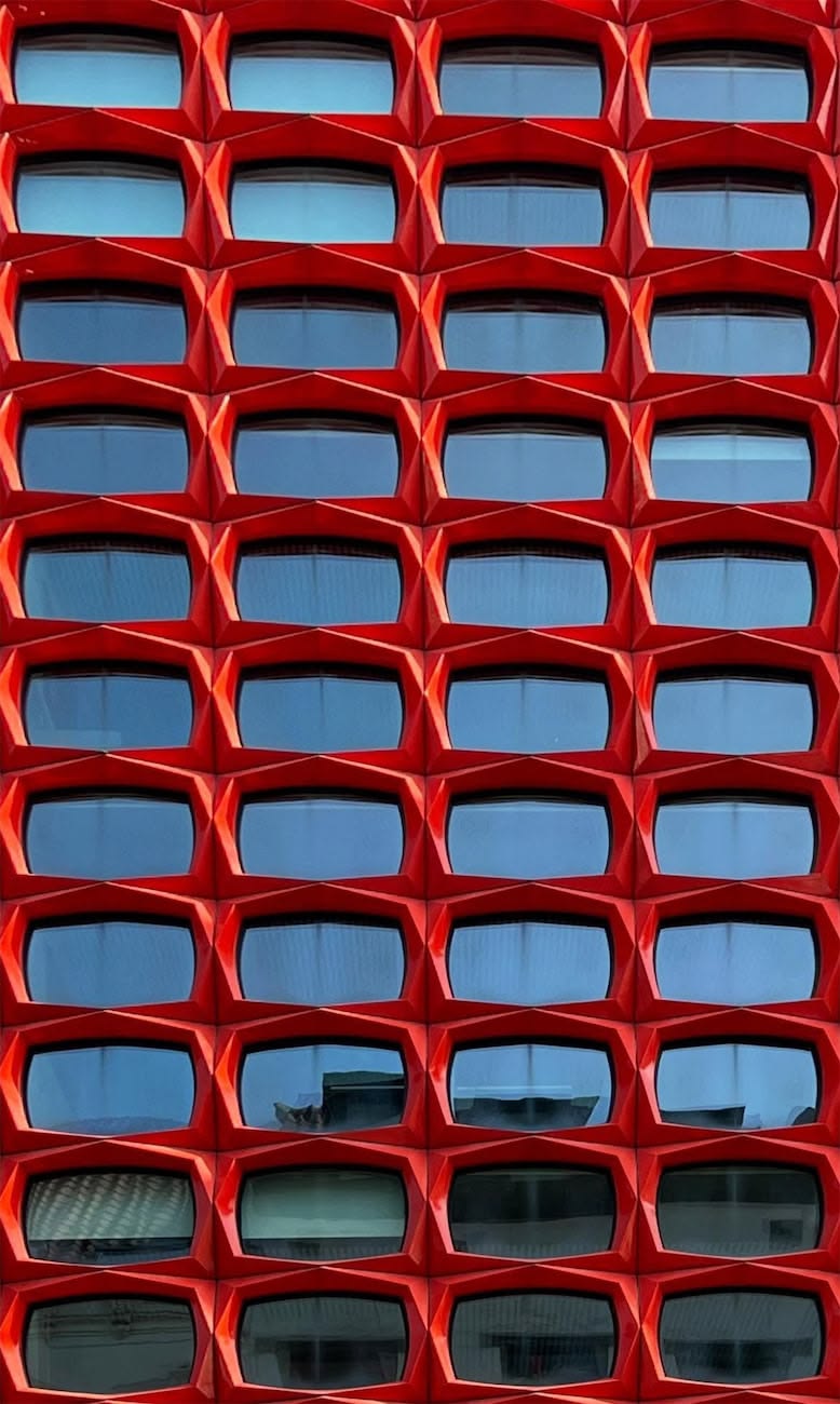 Façade d’un bâtiment avec des fenêtres encadrées de formes géométriques rouges répétées.