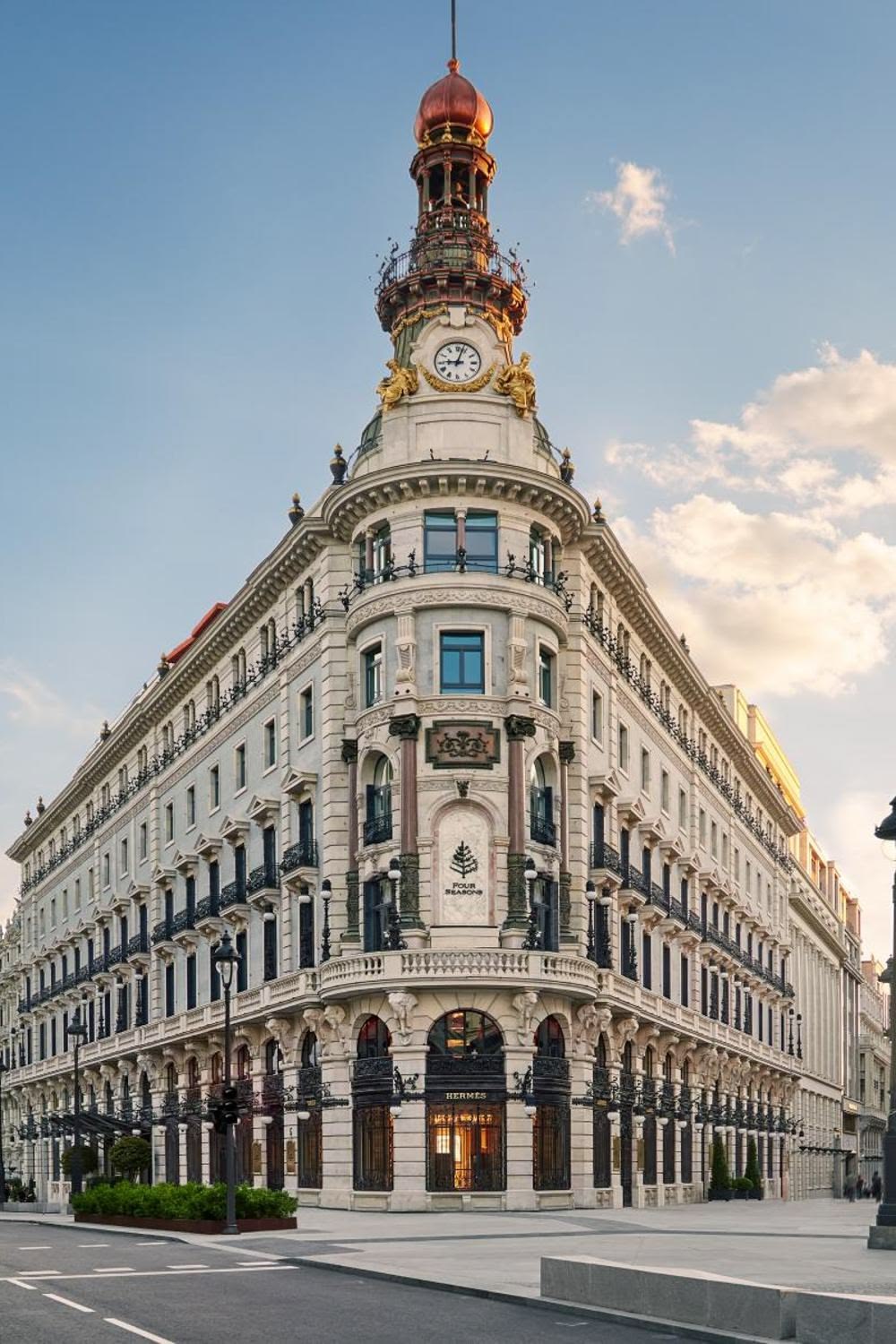 Bâtiment classique avec horloge et enseigne Four Seasons, boutique Hermès au rez-de-chaussée.
