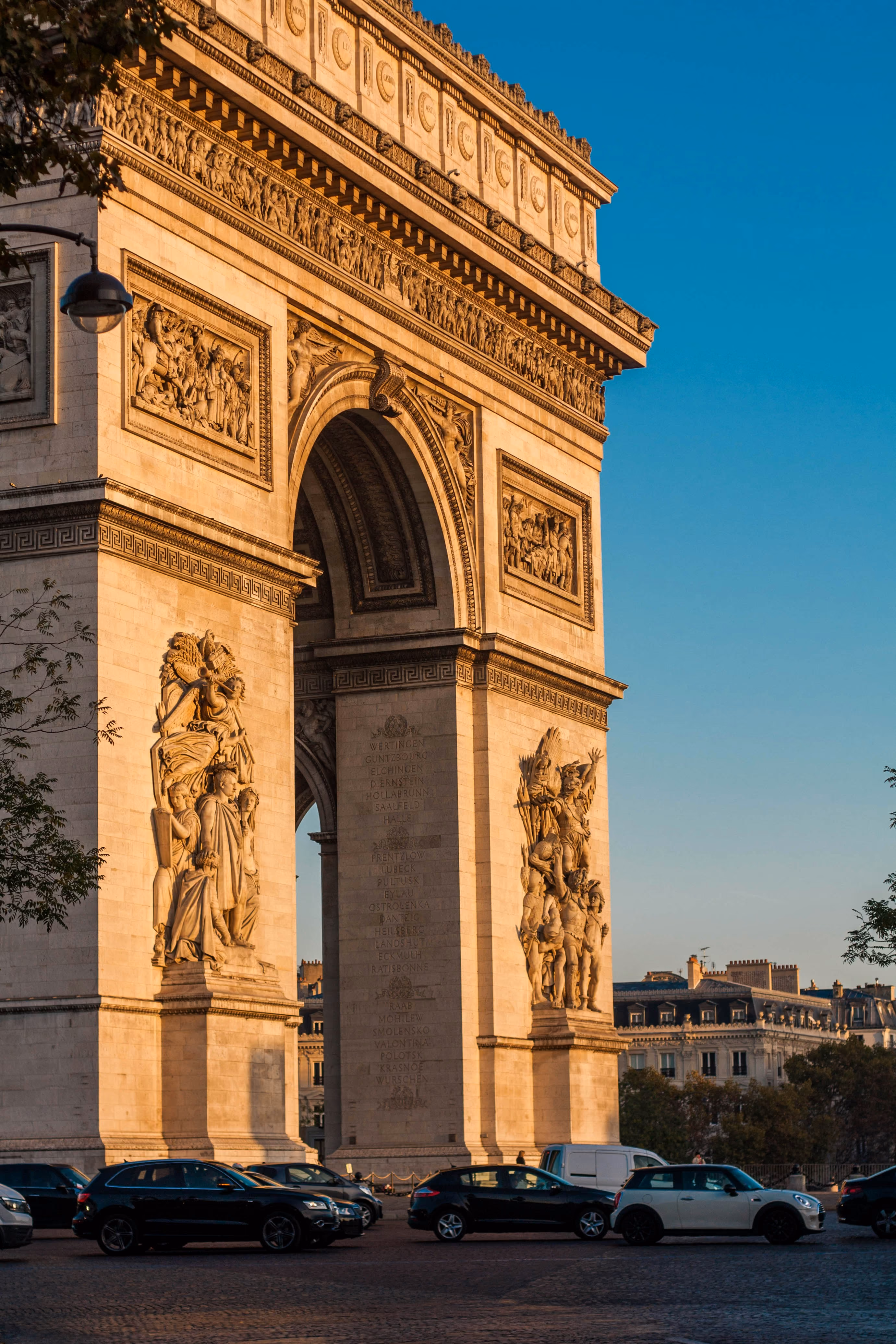 Arc de Triomphe à Paris éclairé par le soleil couchant avec voitures garées devant.