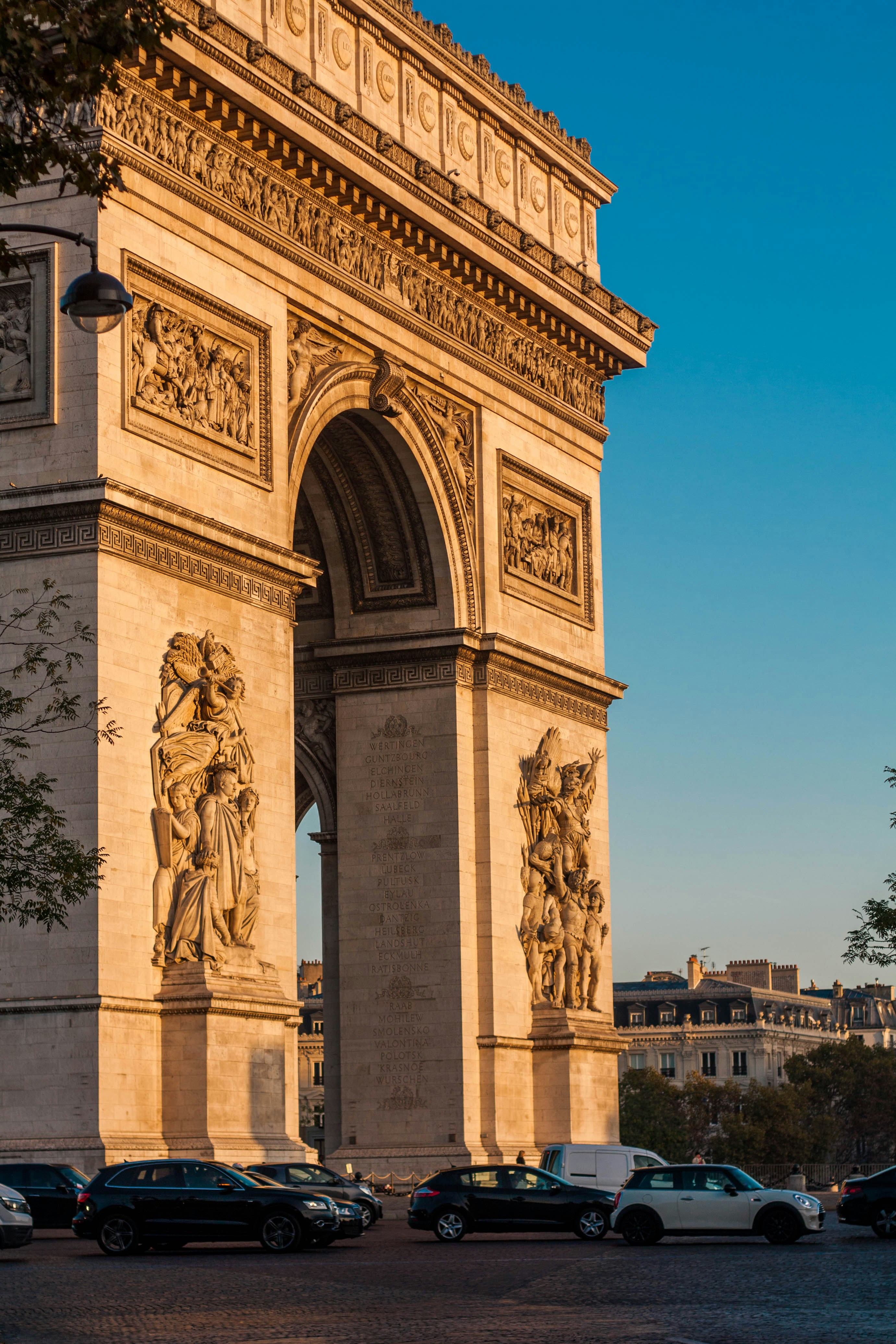 Arc de Triomphe à Paris éclairé par le soleil couchant avec voitures garées devant.
