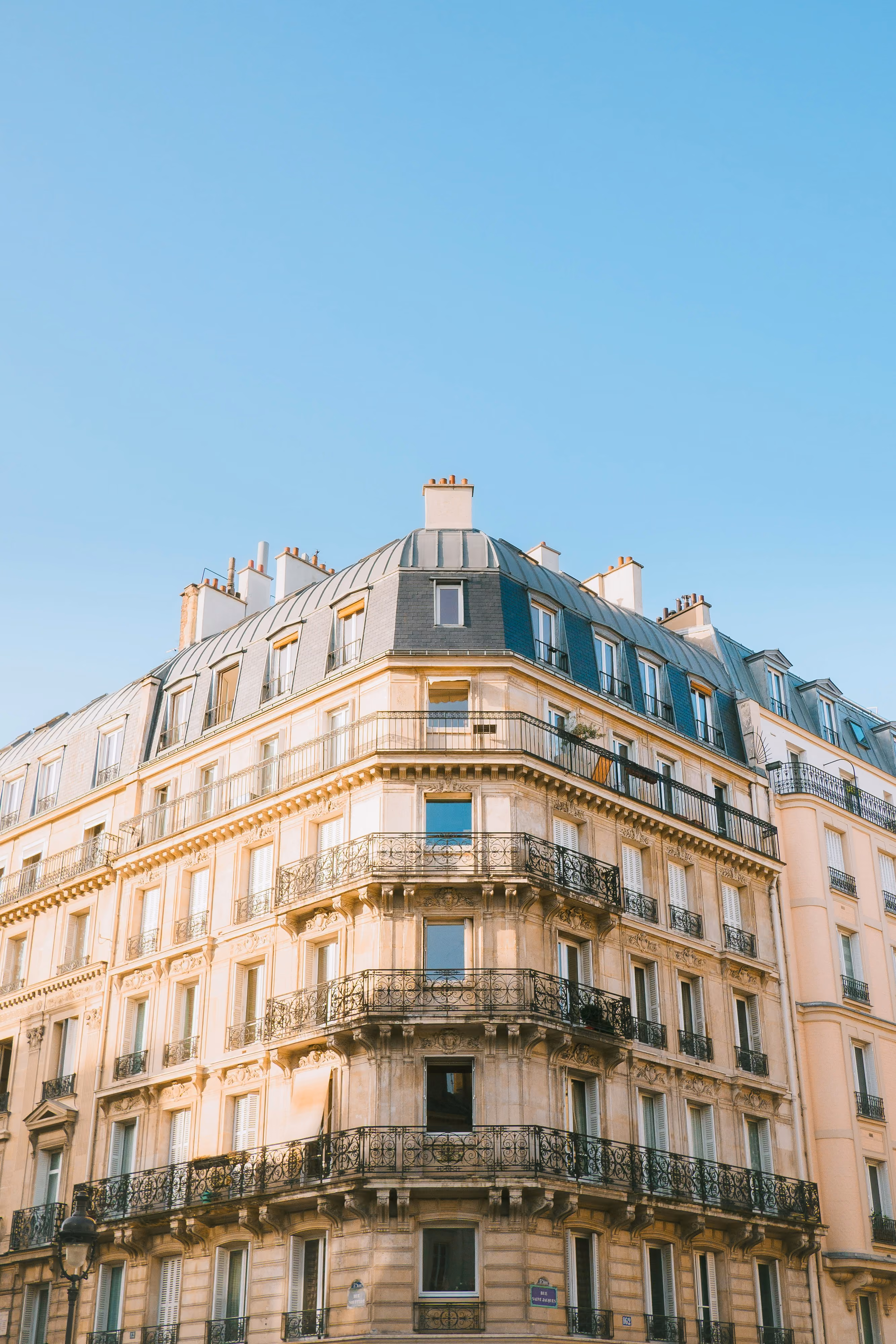 Bâtiment haussmannien parisien avec balcons en fer forgé sous un ciel bleu clair.