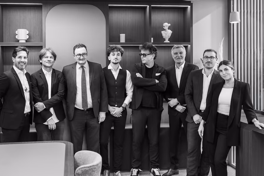 Groupe de huit personnes en tenue professionnelle dans un bureau moderne avec étagères décoratives.