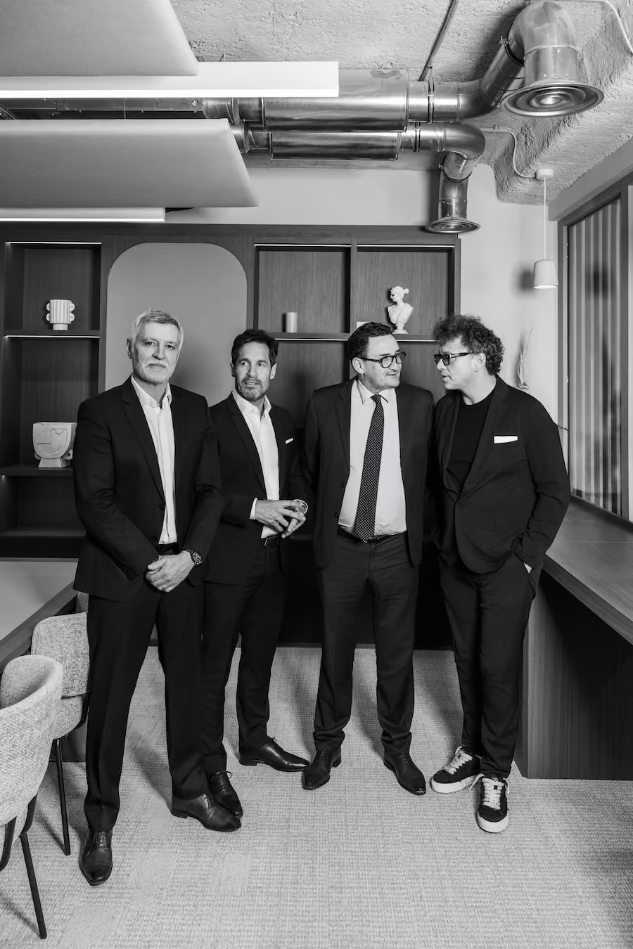 Portrait noir et blanc de quatre hommes en costume dans un bureau avec étagères
