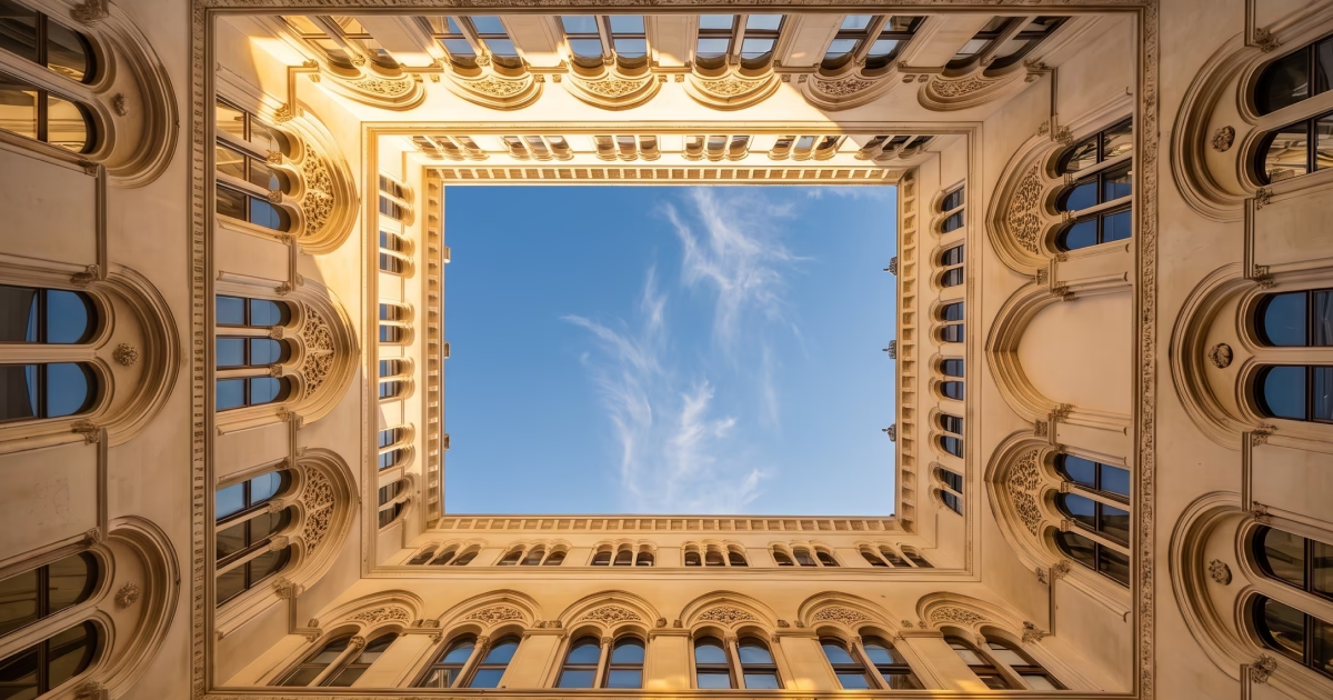 Vue vers le ciel au centre d'une cour carrée entourée de murs ornés de fenêtres gothiques.