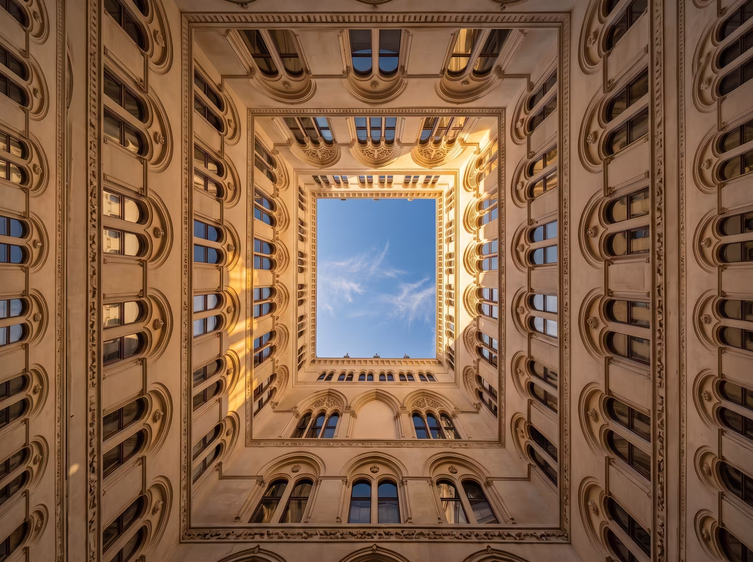 Vue en plongée d'une cour intérieure carrée avec des fenêtres gothiques et ciel bleu.