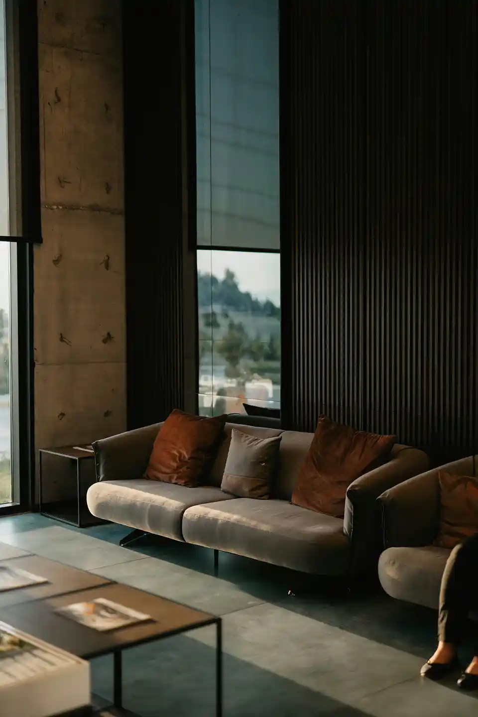 Modern living room with gray sofa, brown cushions, glass window, black panel wall, and coffee table.