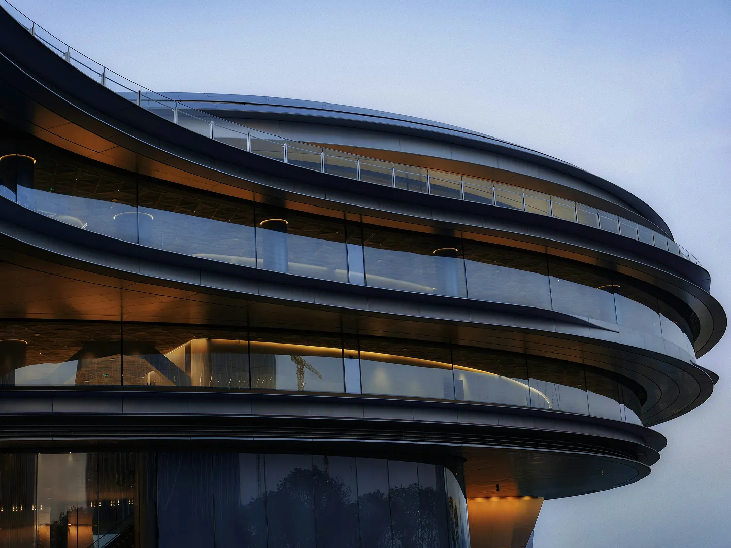 Curved modern building facade with glass walls and warm interior lighting at dusk.