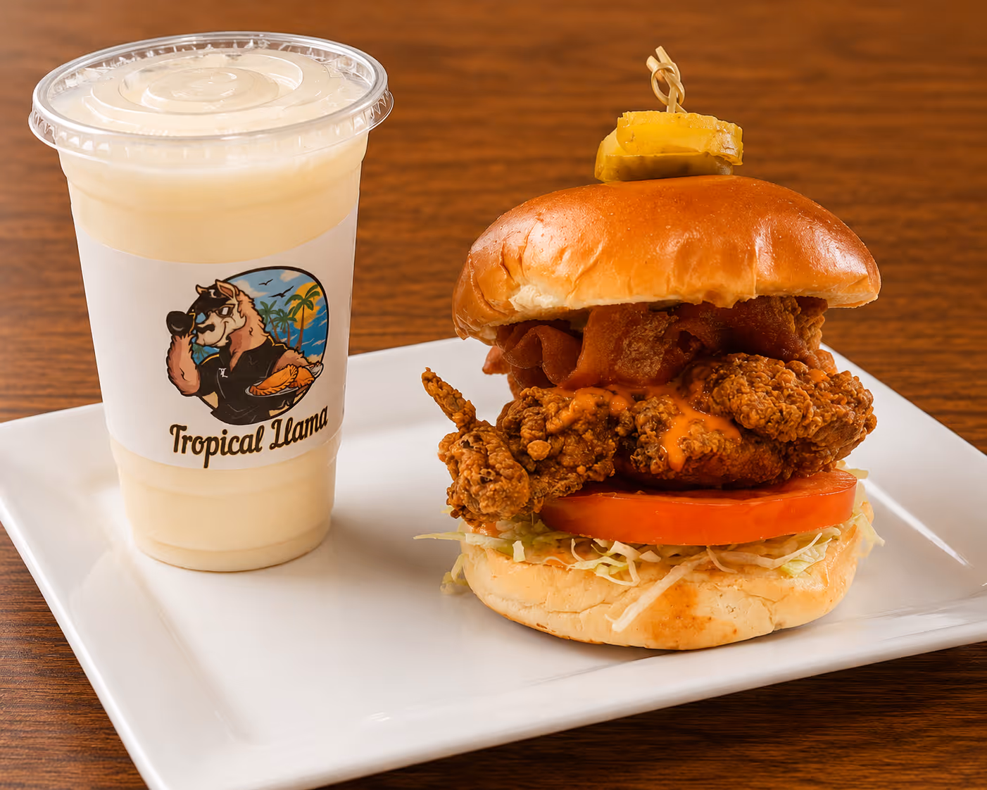 A chicken sandwich with lettuce and tomato, accompanied by a drink, served on a white plate.