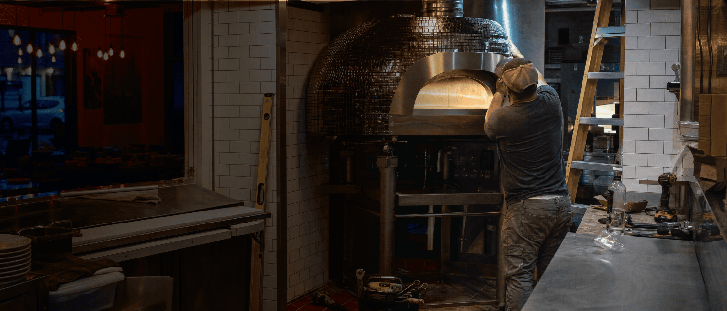 A cook tending a wood-fired pizza oven in a restaurant kitchen