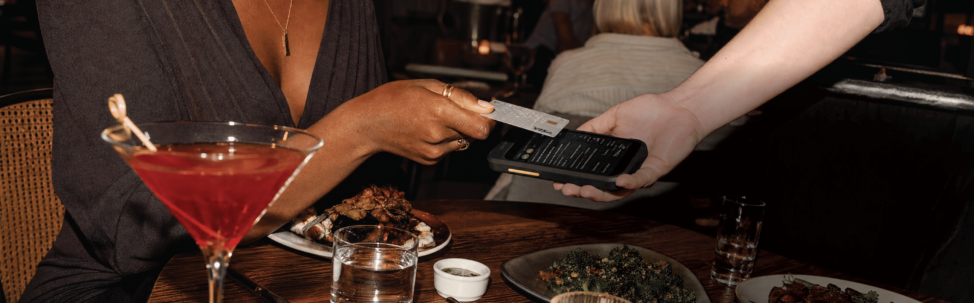 A guest tapping a card to pay at the table while a server holds a handheld reader