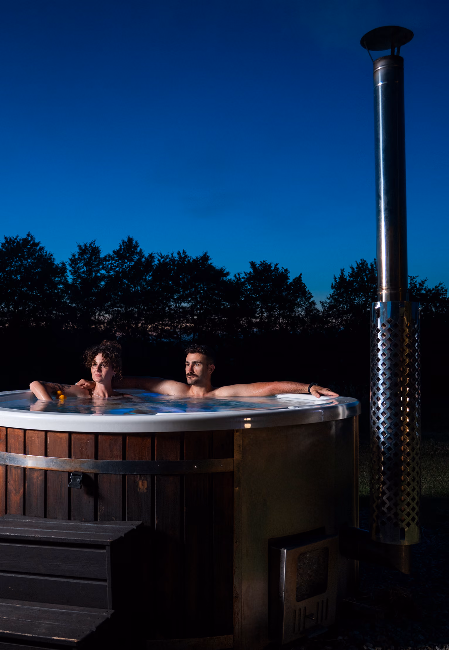 Una coppia immersa nel proprio Hot tub (jacuzzi o bagno caldo) fuori dalla propria yurta al Glamping per coppie Due cuori e una Yurta