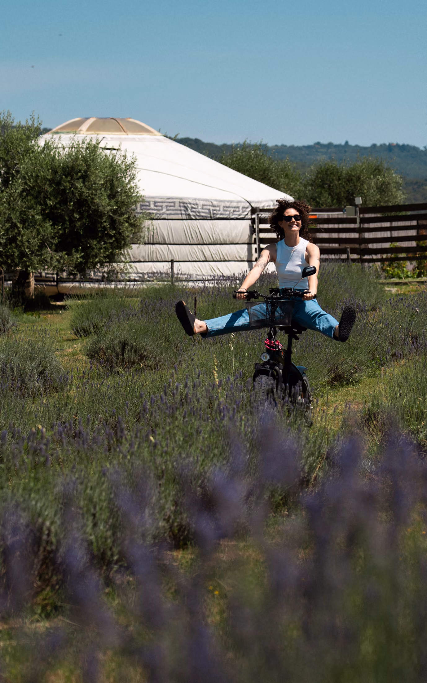 Una ragazza sorridente pedala su una bici elettrica nei campi di lavanda fuori dalle yurte del Glamping per coppie Due cuori e una Yurta