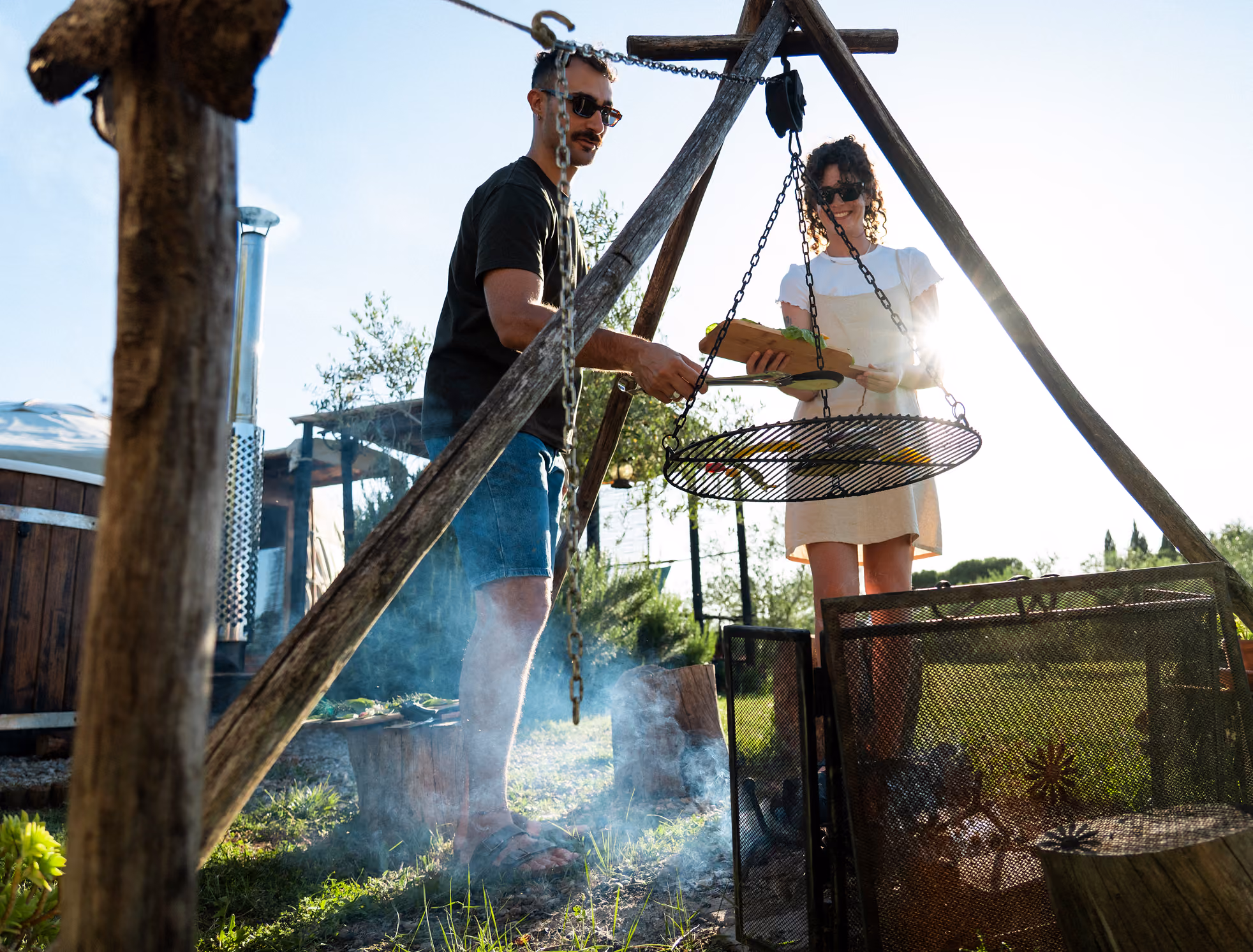 Una coppia griglia del cibo sul barbecue (bbq, falò) fuori dalla propria yurta al Glamping per coppie Due cuori e una Yurta