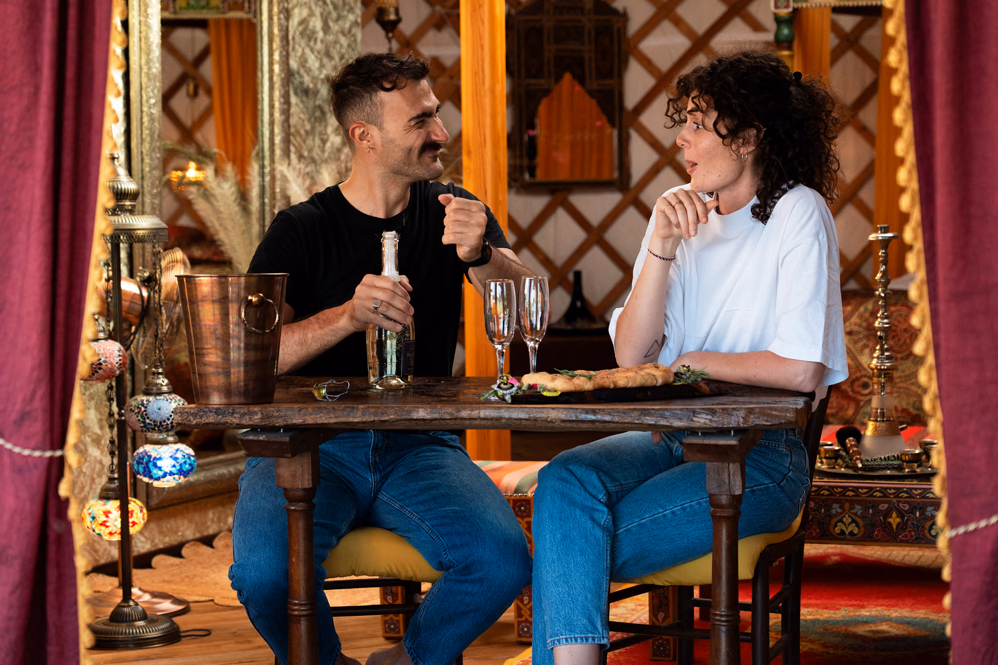 Una coppia stappa una bottiglia di prosecco, parte del proprio benvenuto romantico al Glamping per coppie Due cuori e una Yurta