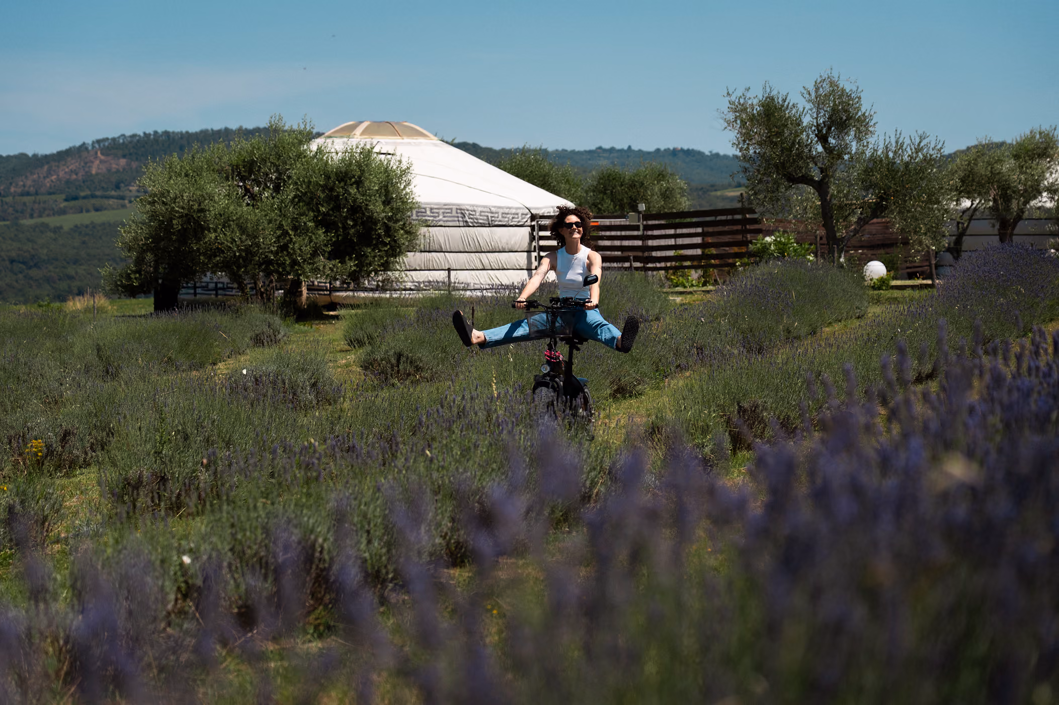 Una ragazza pedala su una bici elettrica in mezzo alla natura, con sfondo una yurta del Glamping per coppie Due cuori e una Yurta