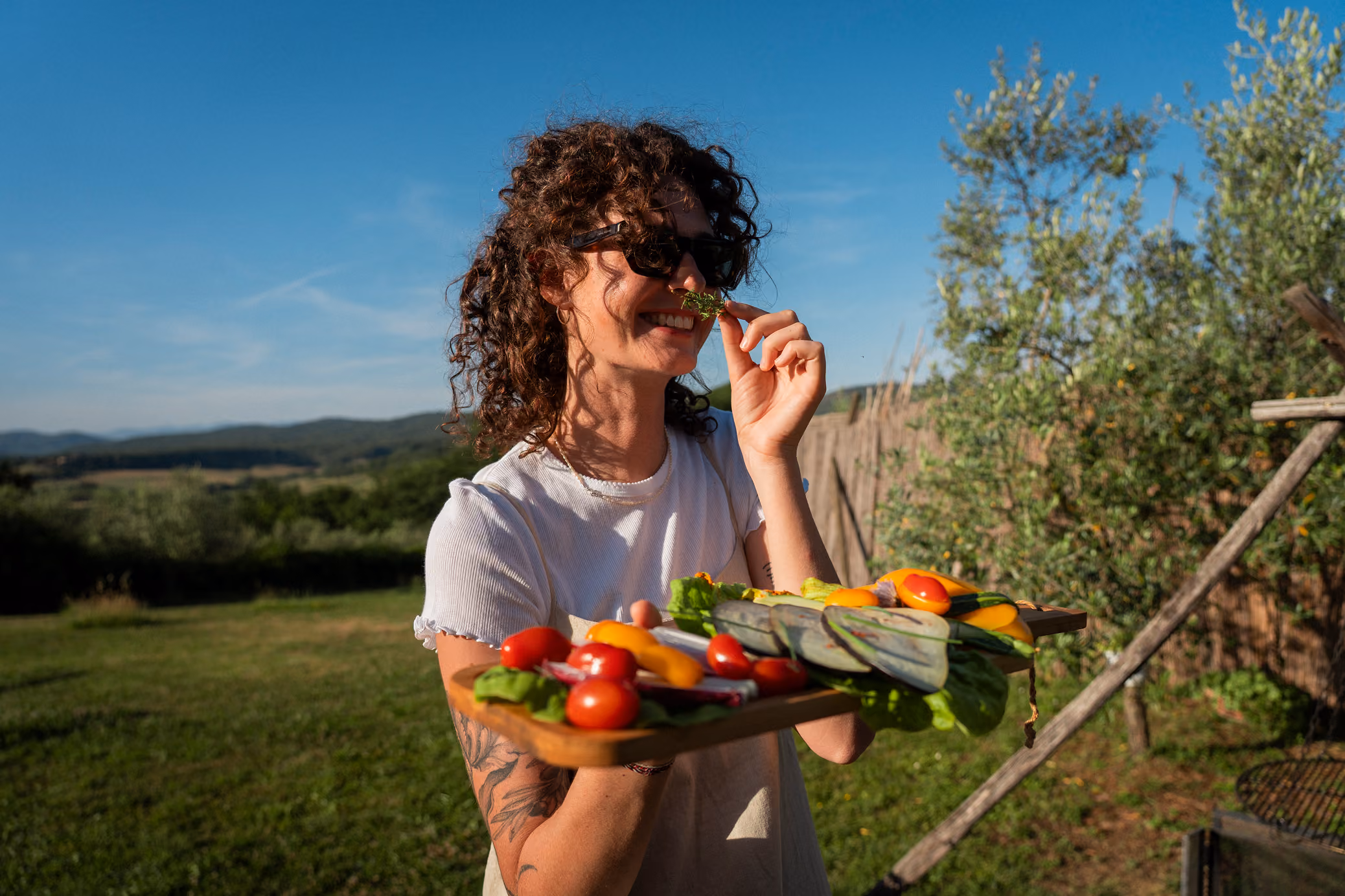 Una ragazza sorridente porge un tagliere di verdure da grigliare al barbecue (bbq, falò) fuori dalla yurta al Glamping per coppie Due cuori e una Yurta