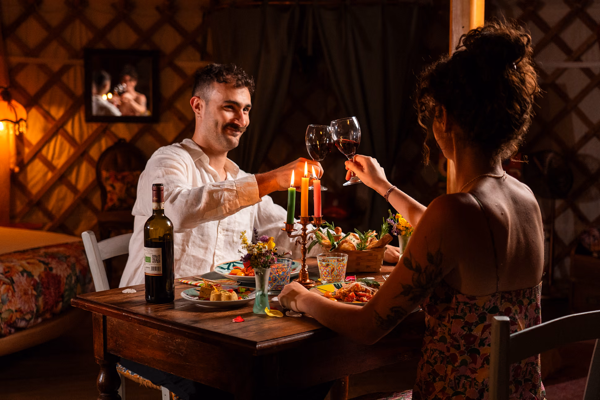 Una coppia condivide una cena romantica organica, facendo un brindisi dentro la propria yurta al Glamping per coppie Due cuori e una Yurta