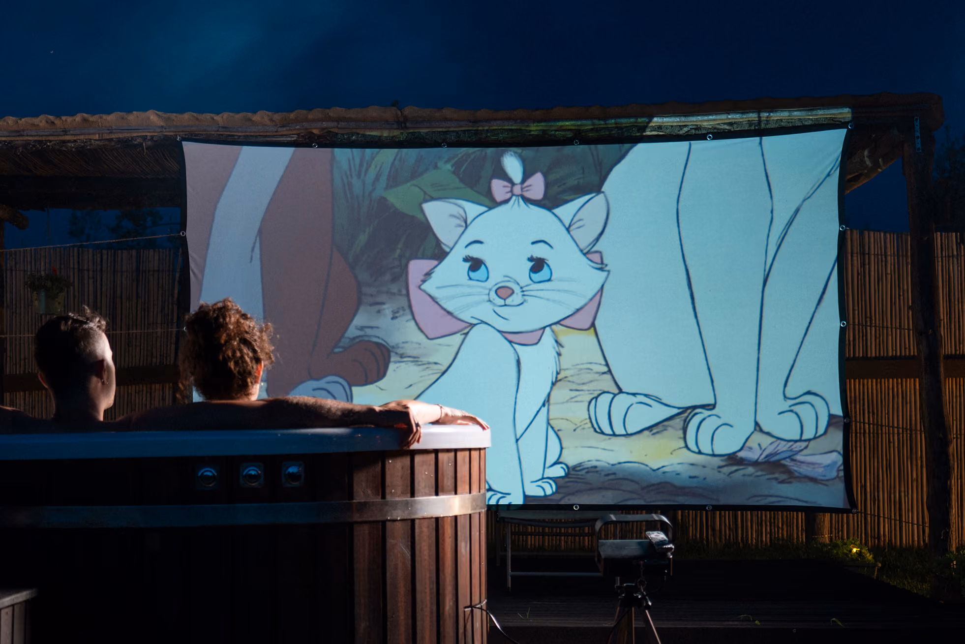 Una coppia guarda un film del cinema privato, immersa nell'hot tub (Jacuzzi o bagno caldo) al Glamping per coppie Due cuori e una Yurta