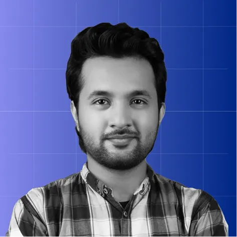 Portrait of a man with dark hair and beard wearing a plaid shirt against a blue gradient background.