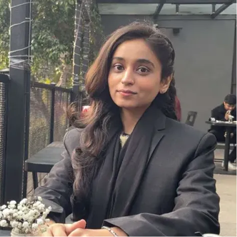 Young woman with long dark hair sitting at an outdoor café table with flowers in view.