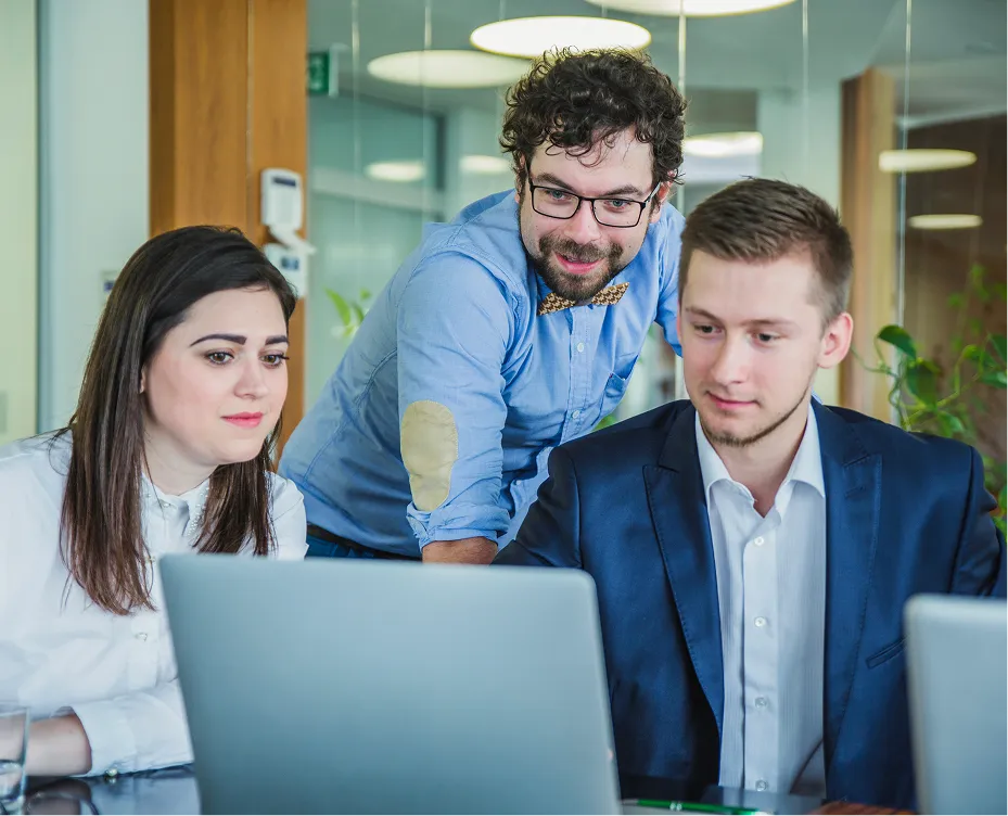 Three colleagues collaborating and looking at a laptop screen in a modern office setting.