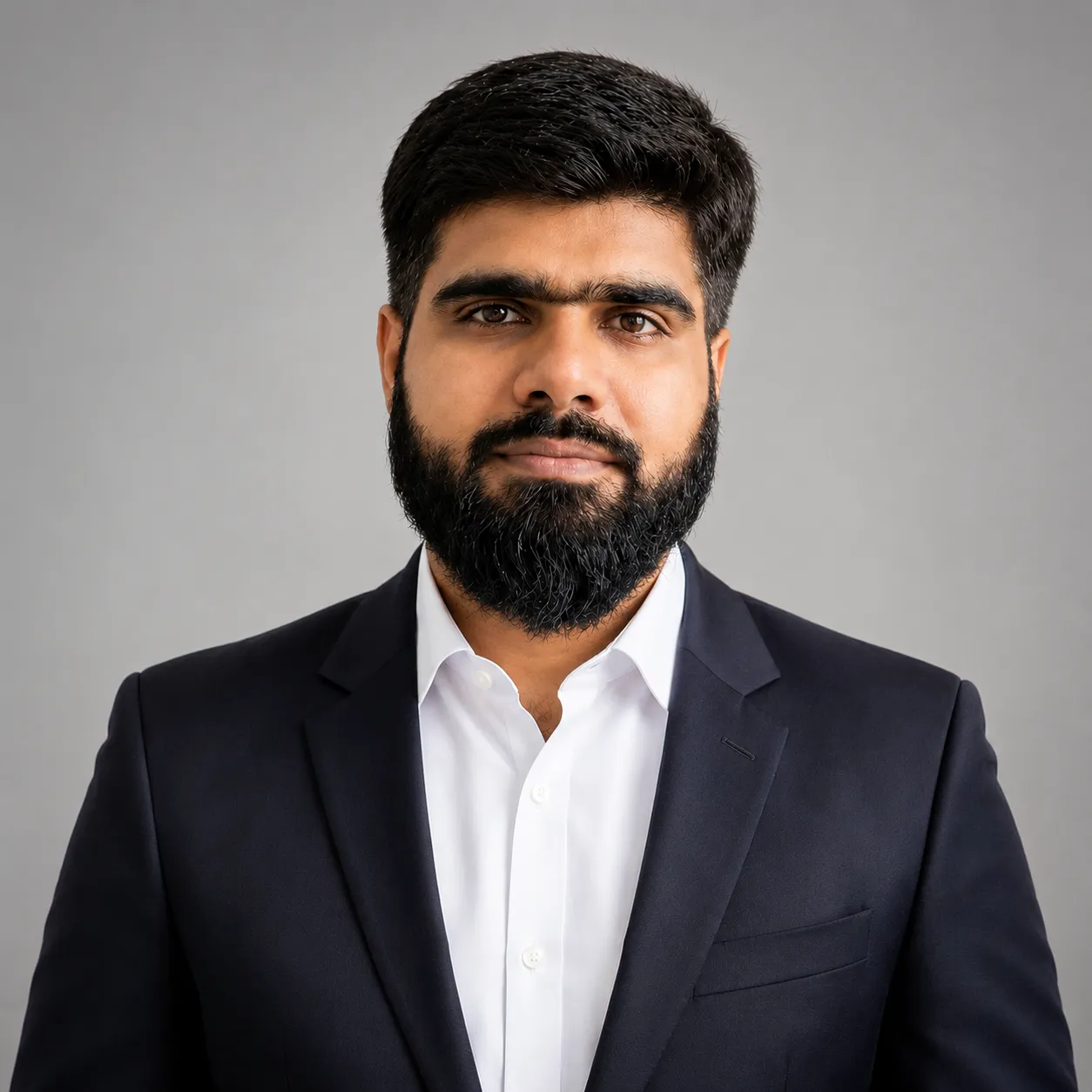 Portrait of a man with a beard wearing a white traditional buttoned shirt against a plain background.