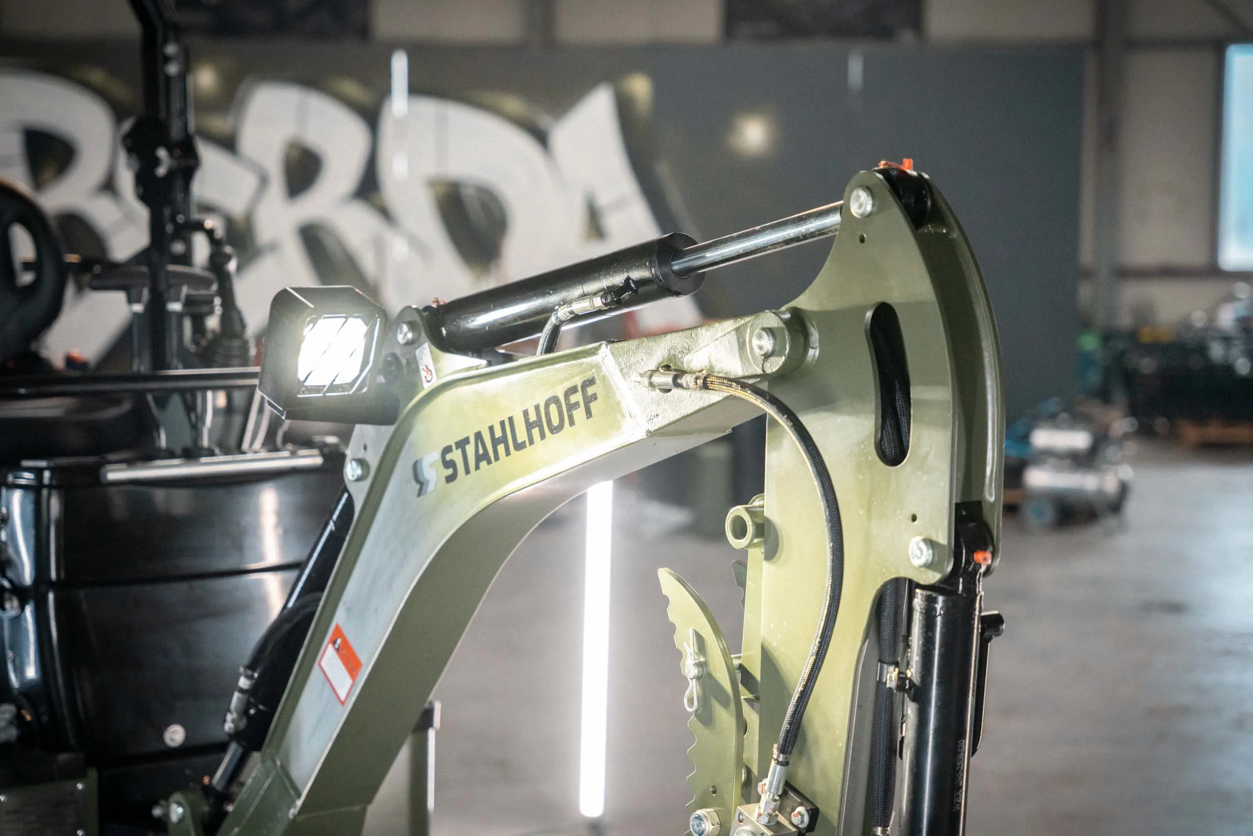 Traktor transportiert im Stall eine große Rundballen-Heuballen, während Kühe in ihren Boxen stehen.