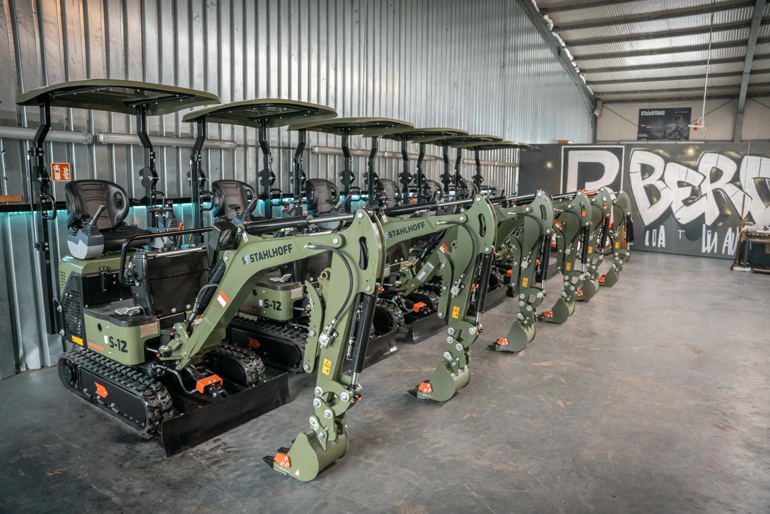 Traktor transportiert im Stall eine große Rundballen-Heuballen, während Kühe in ihren Boxen stehen.