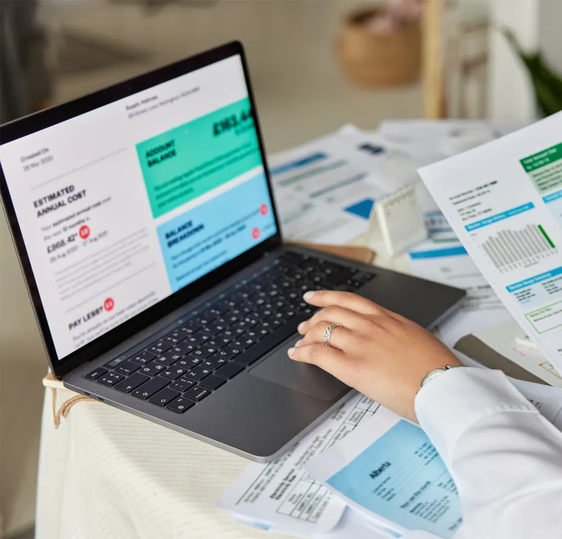 Hand with rings on a laptop keyboard with financial documents and reports on the table.