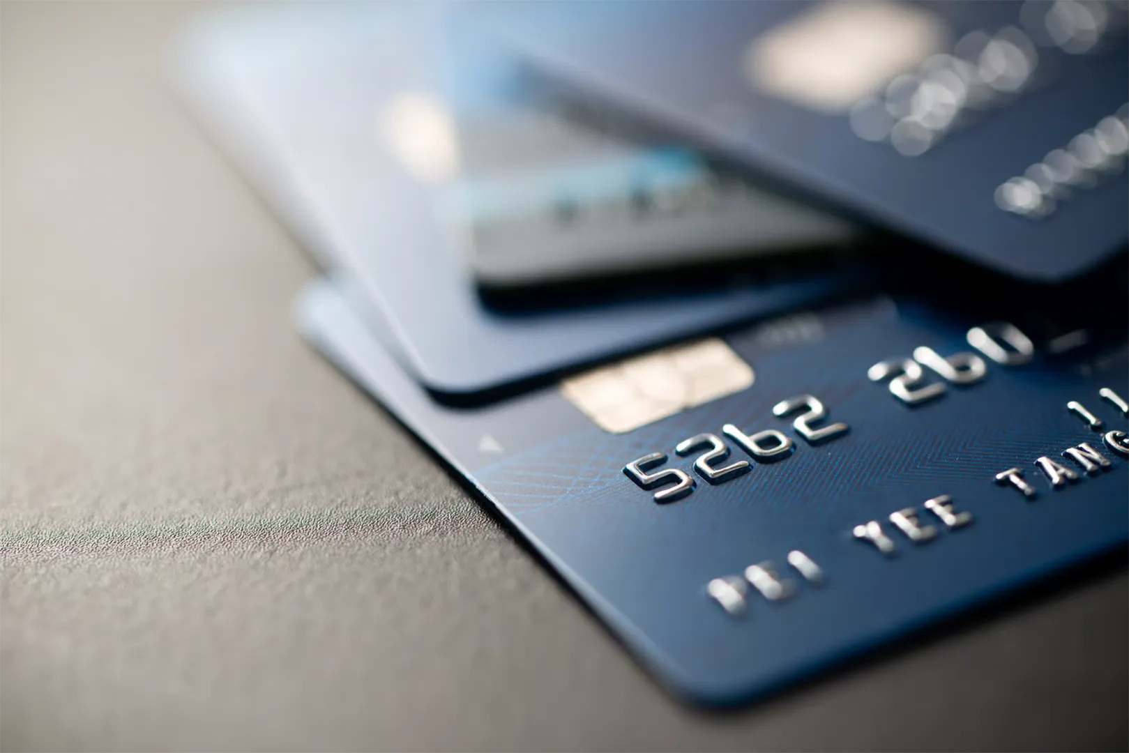 Close-up of three stacked blue credit cards on a gray surface with visible card chip and numbers.