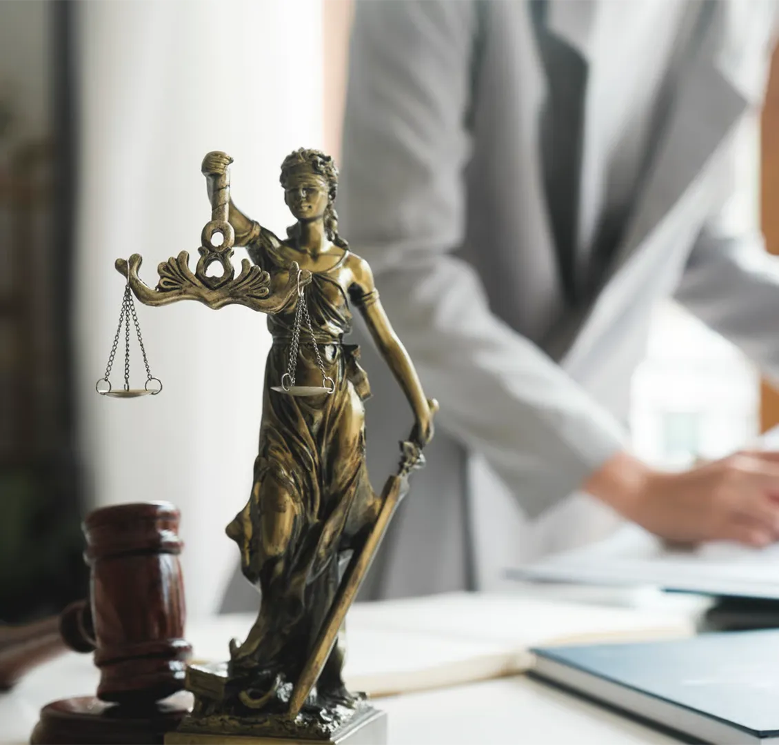 Bronze Lady Justice statue holding scales and sword with blurred person and gavel in background.
