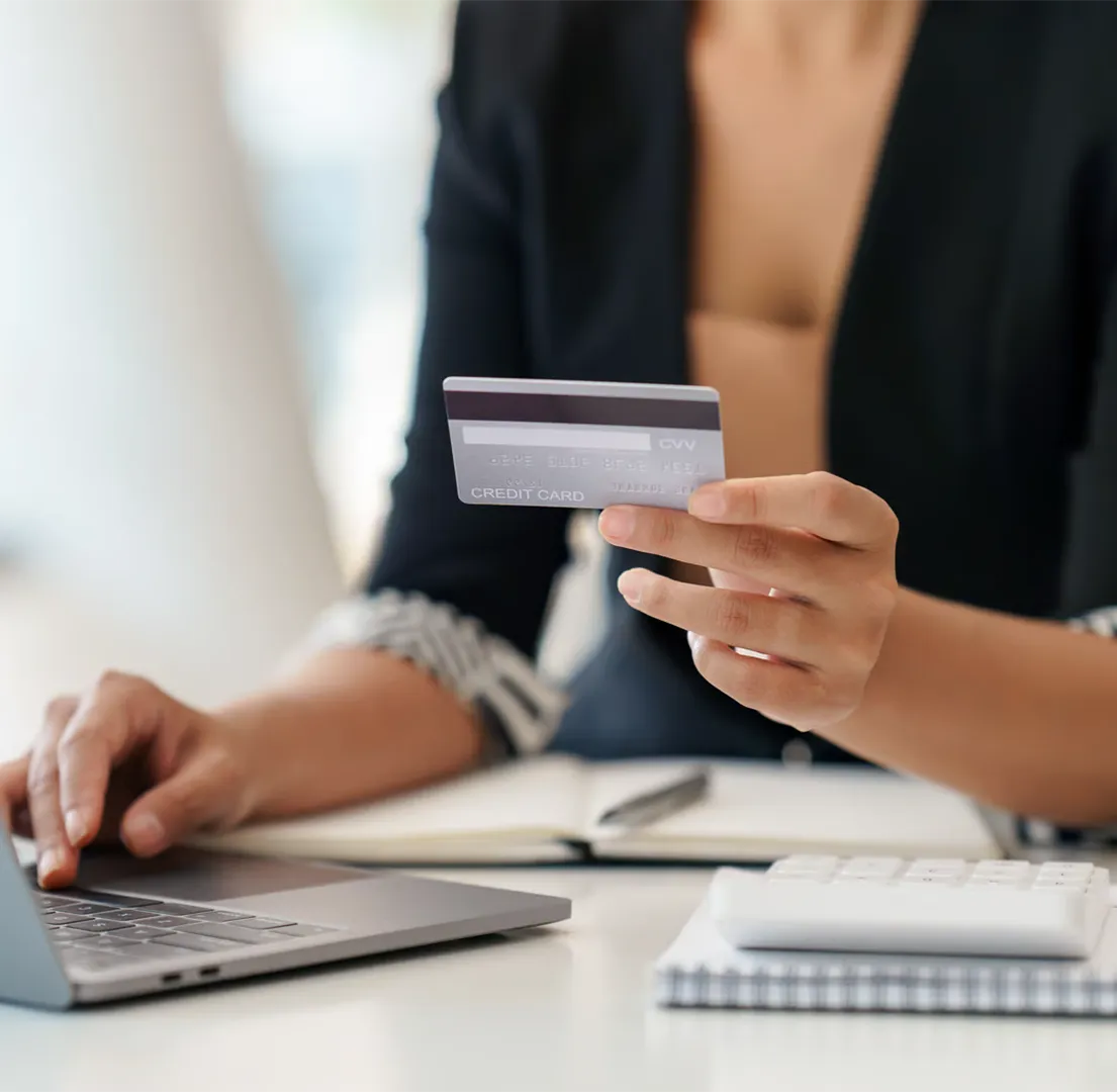 Person holding a credit card and using a laptop at a desk with a notebook and calculator.
