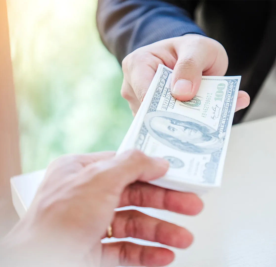 Close-up of one person handing US hundred-dollar bills to another person.